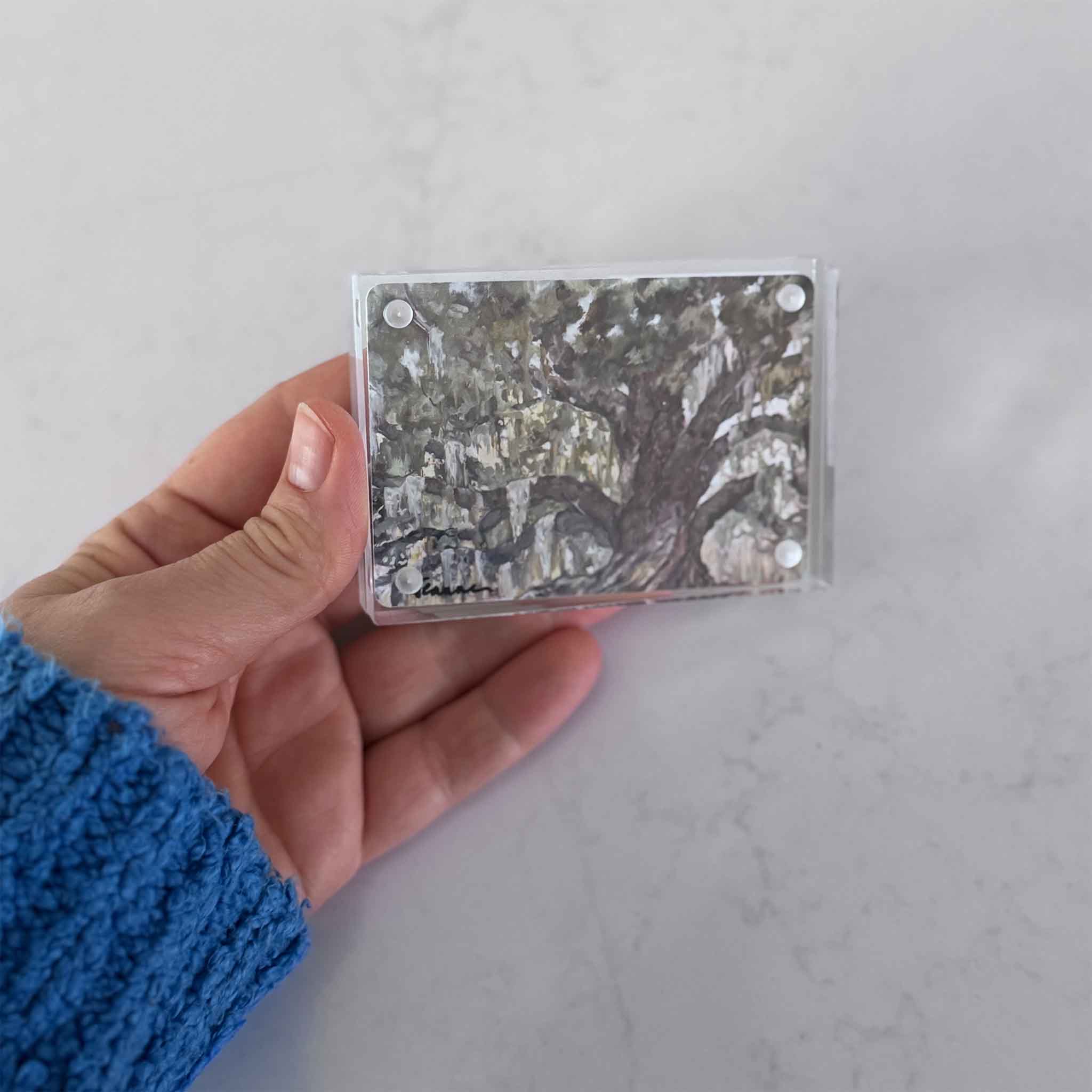 Hand holding a small square object with a tree design against a light gray background
