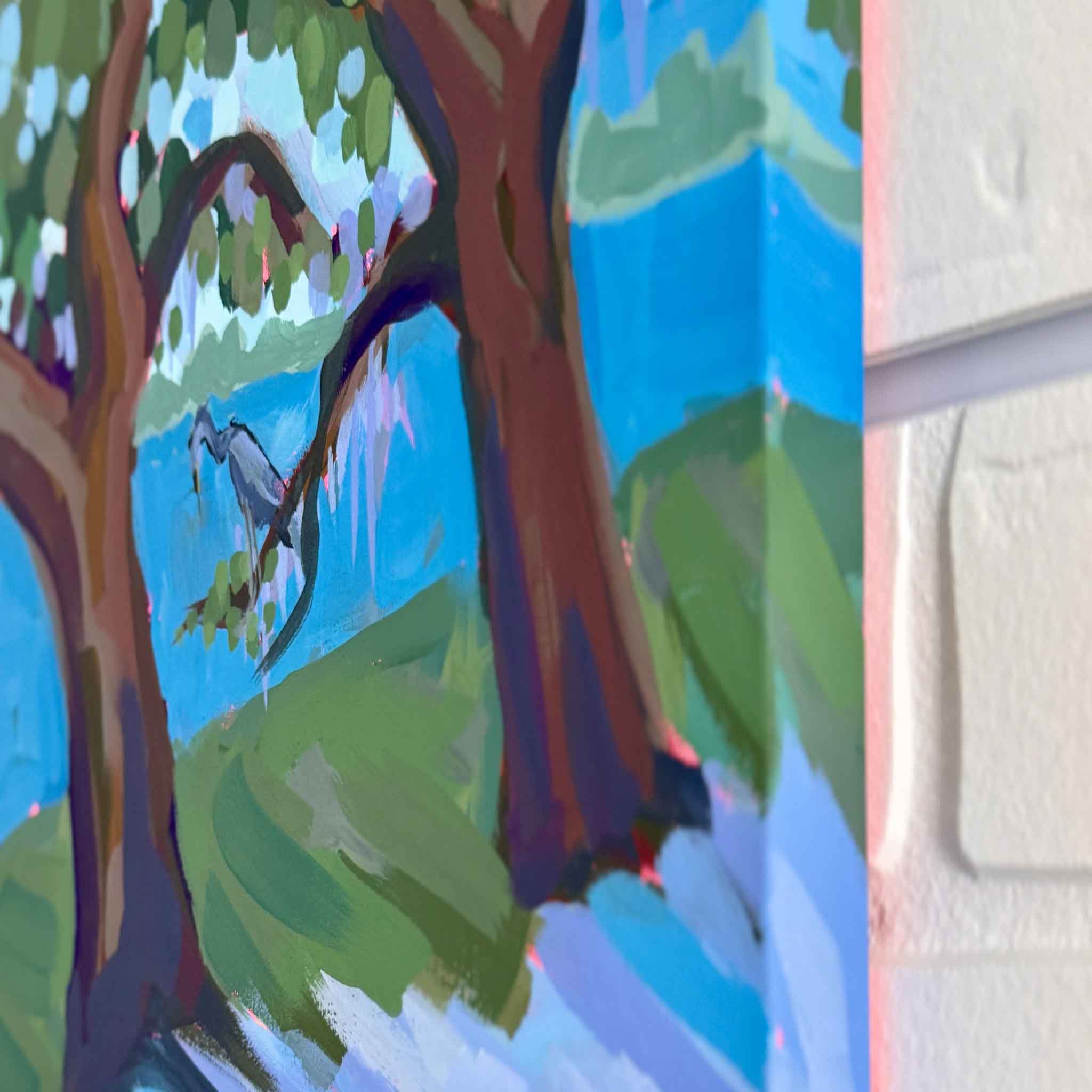 Colorful mixed media artwork of lowcountry trees and water against a white brick wall