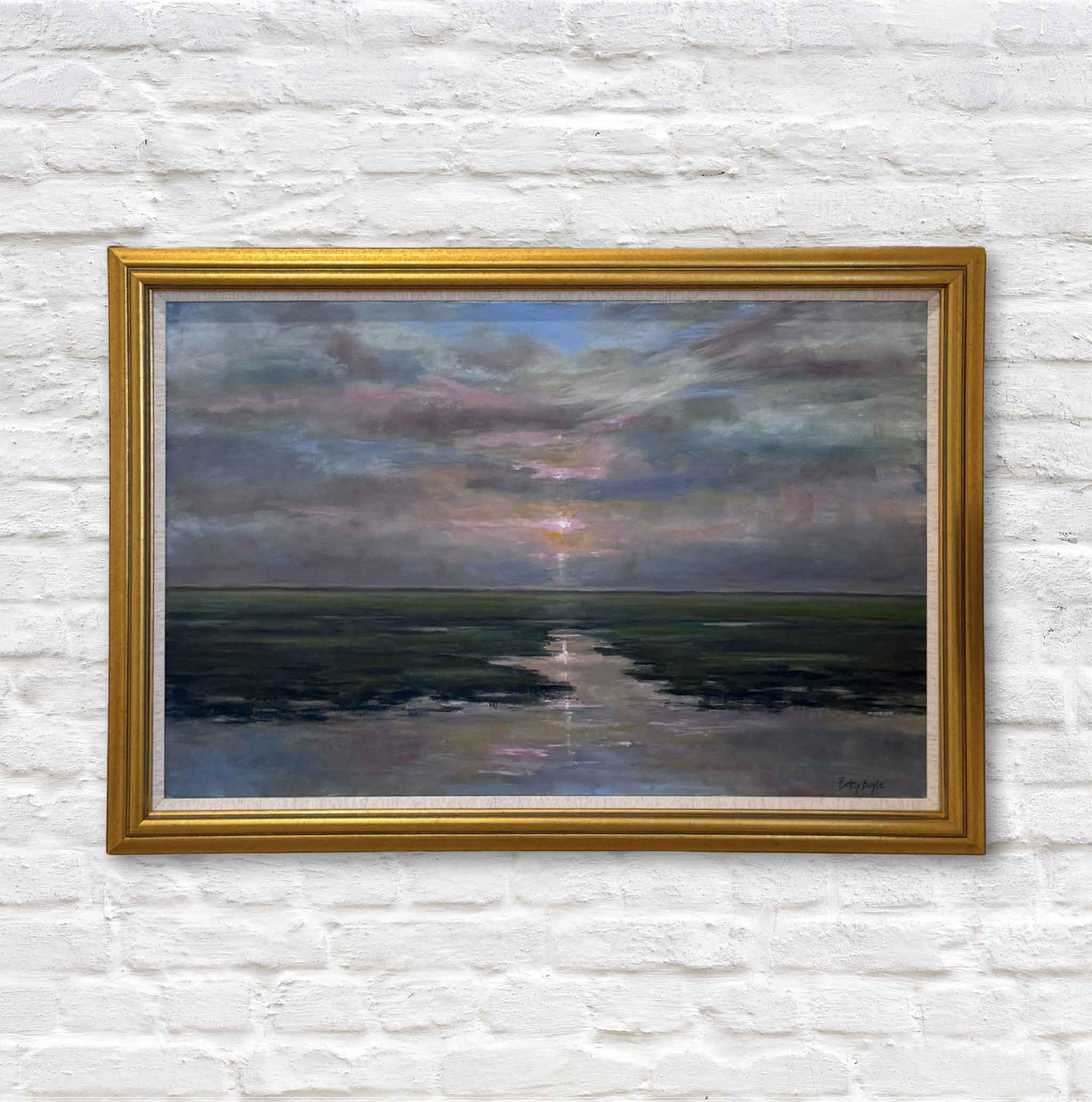 Framed painting of a sunset over water on a white brick wall