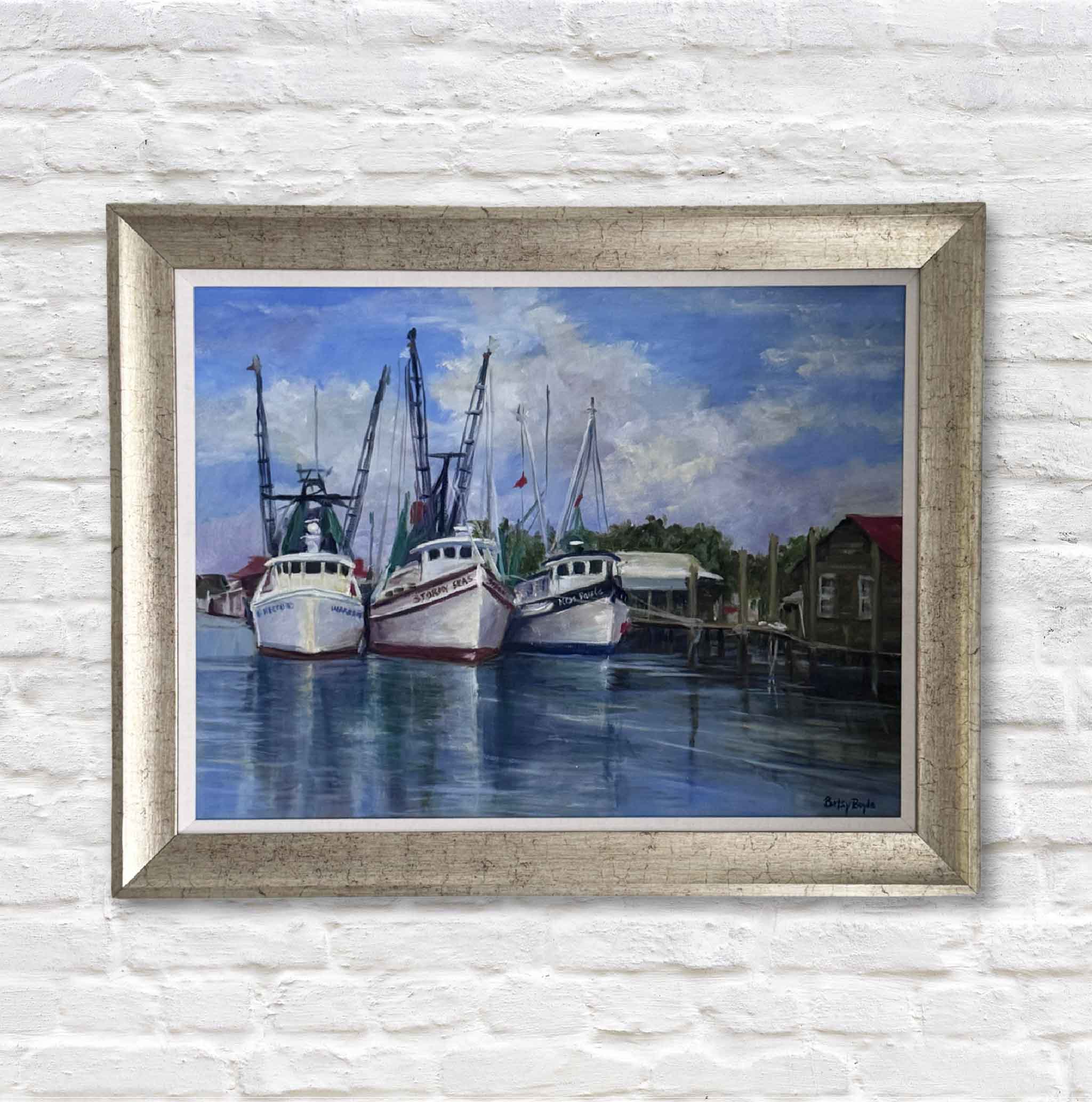 Framed painting of boats docked at a harbor on a white brick wall.