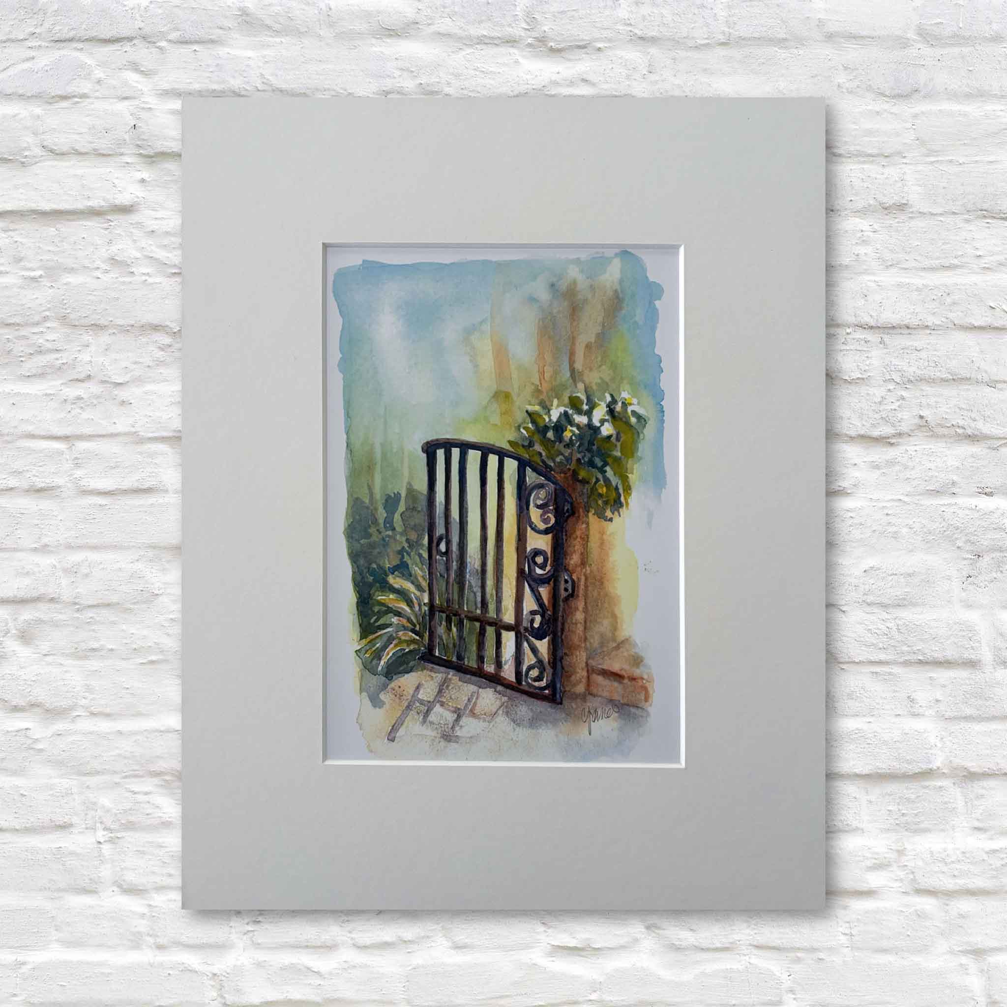matted watercolor painting of a gate with flowers on a white brick wall.