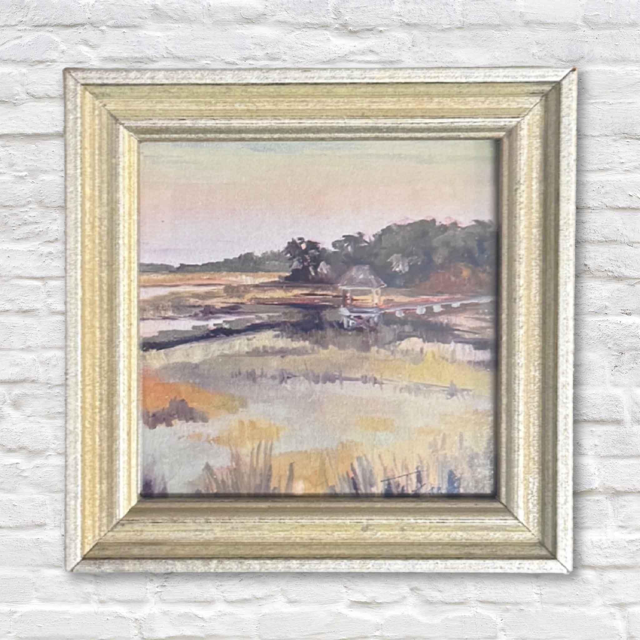 Framed painting of a landscape with a house on a white brick wall