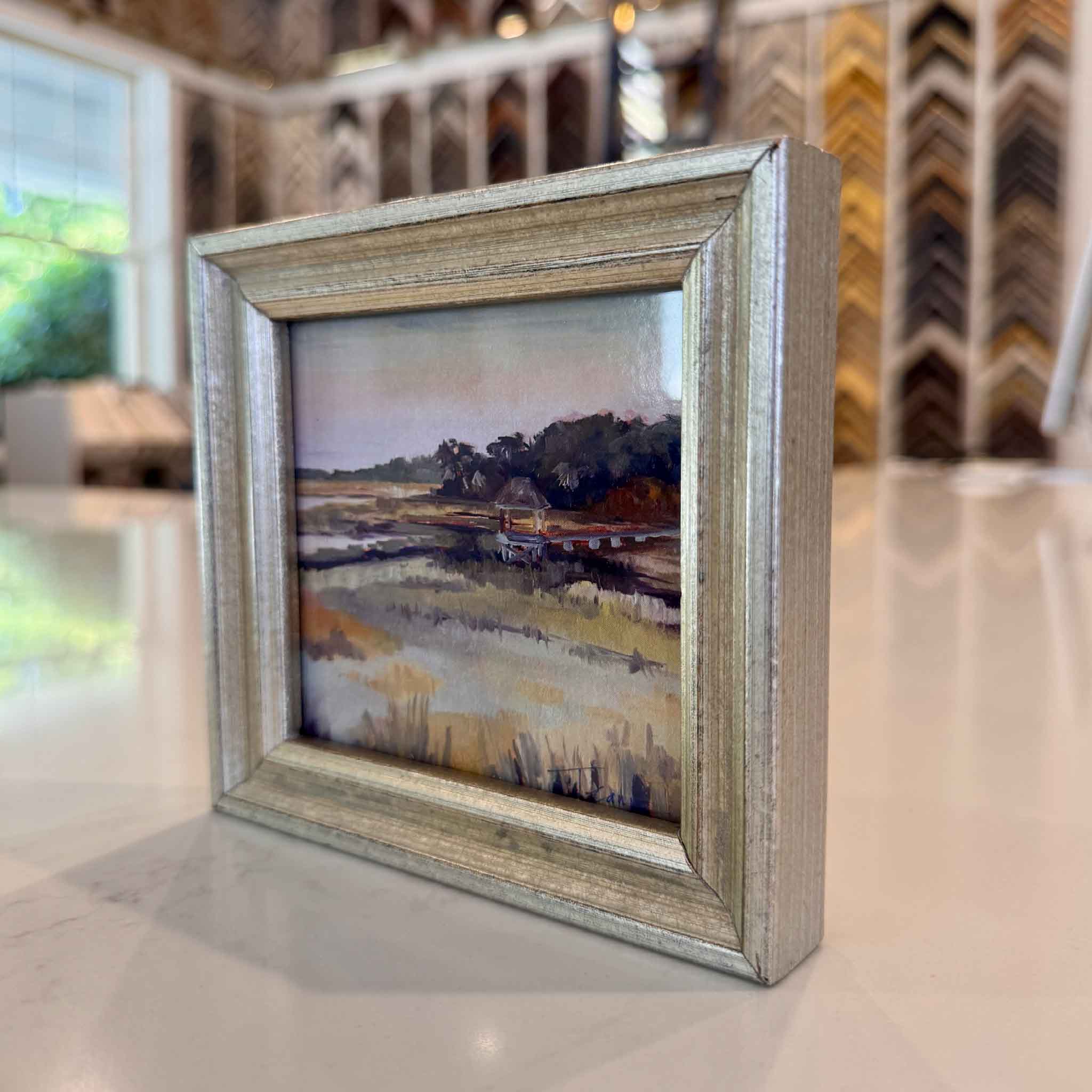 Framed painting of a landscape on a table with a blurred background
