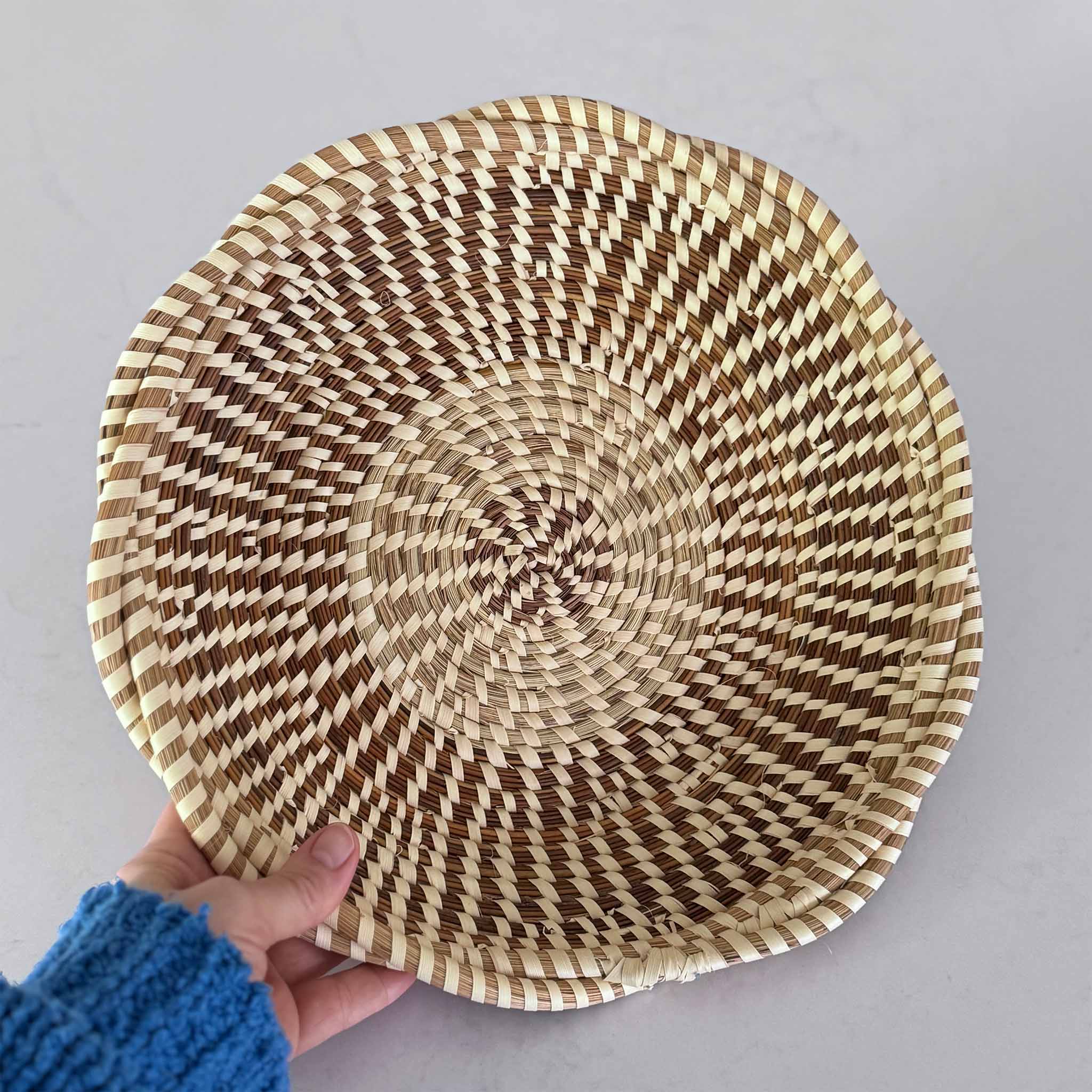 Handwoven Charleston sweetgrass basket with a striped pattern held by a person against a plain background