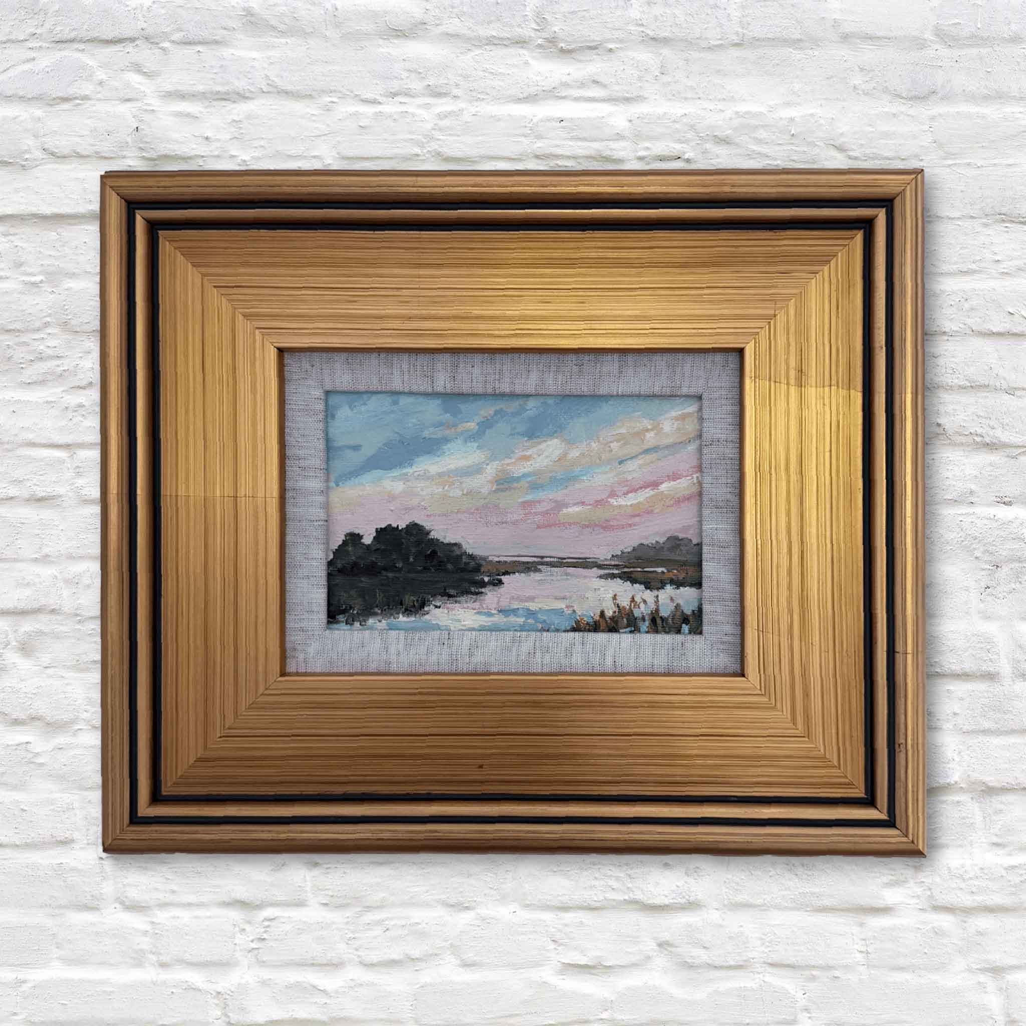 Framed artwork of a landscape with a wooden frame on a textured white wall.