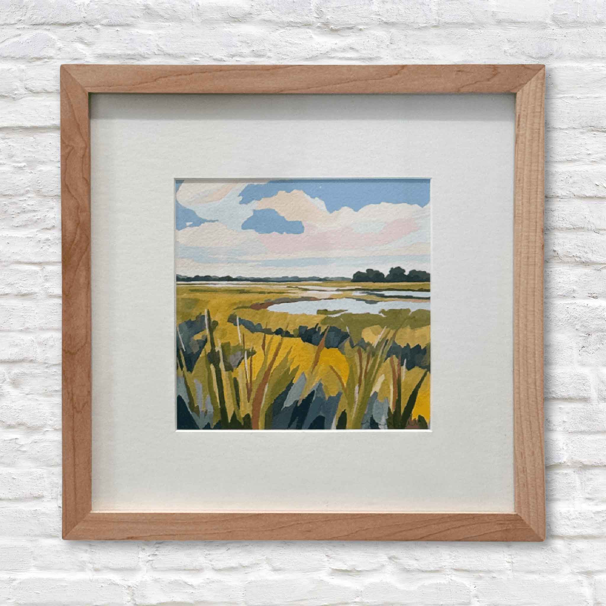 Framed artwork of a landscape with yellow fields and blue sky on a white brick wall.
