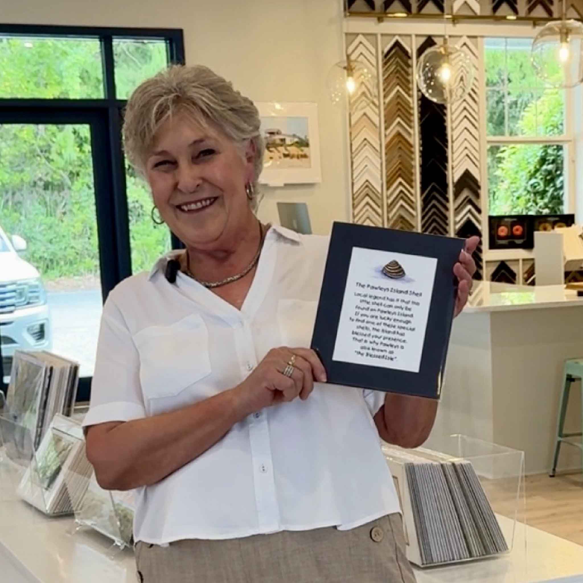 Vida Miller  holding her cherished verse of the Pawleys Island Shell in a frame shop