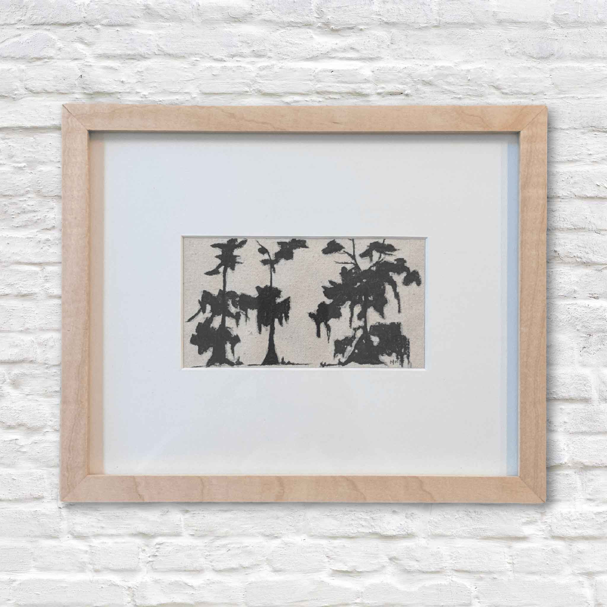 Framed artwork with black abstract design on a white background, mounted on a light gray brick wall.