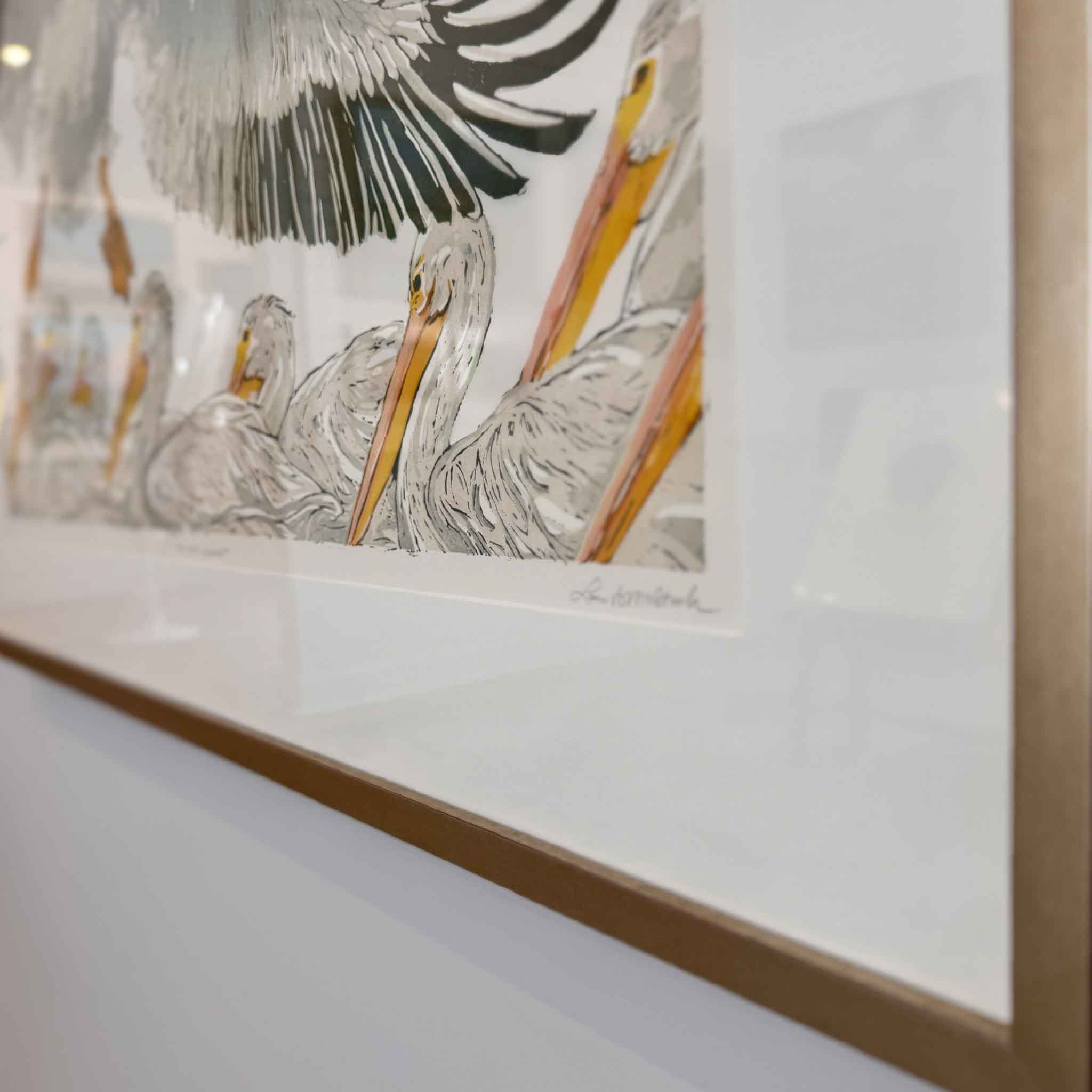 Original linocut reduction print The White Pelicans by Laurie McIntosh, featuring pelicans in flight and water, printed on cotton paper with layered “suicide printing” technique, framed in Laurie’s signature frame.