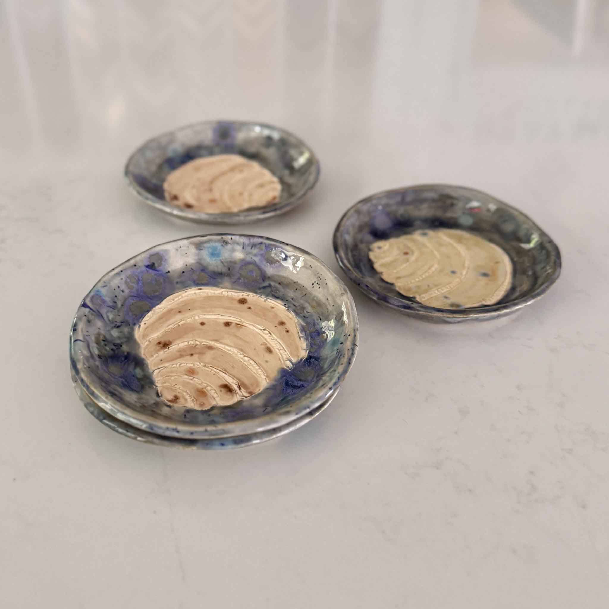 Three ceramic plates with a blue and white glaze, each containing a small amount of beige substance on a white background.