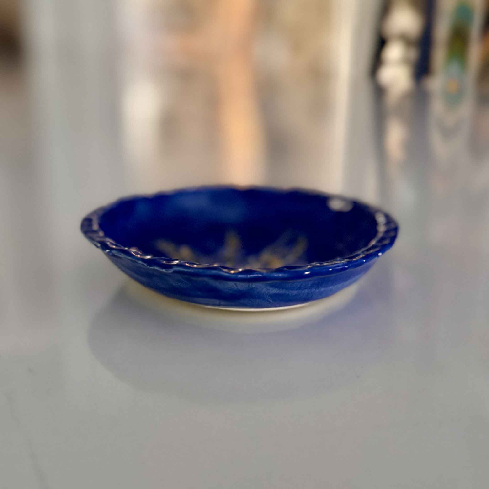 indigo blue pottery plate with gold rice design in center on white brick wall