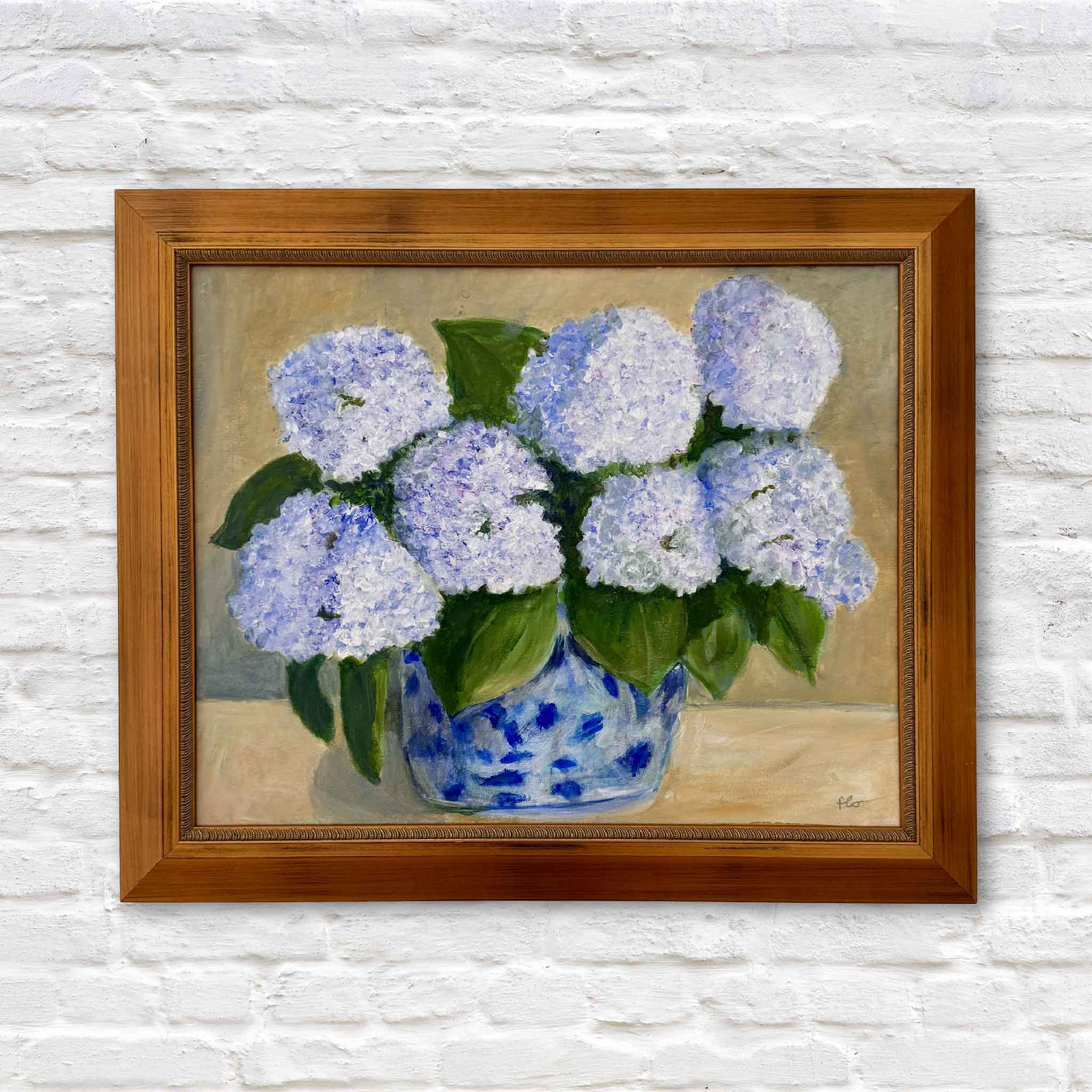 Framed painting of hydrangeas in a blue vase on a white brick wall