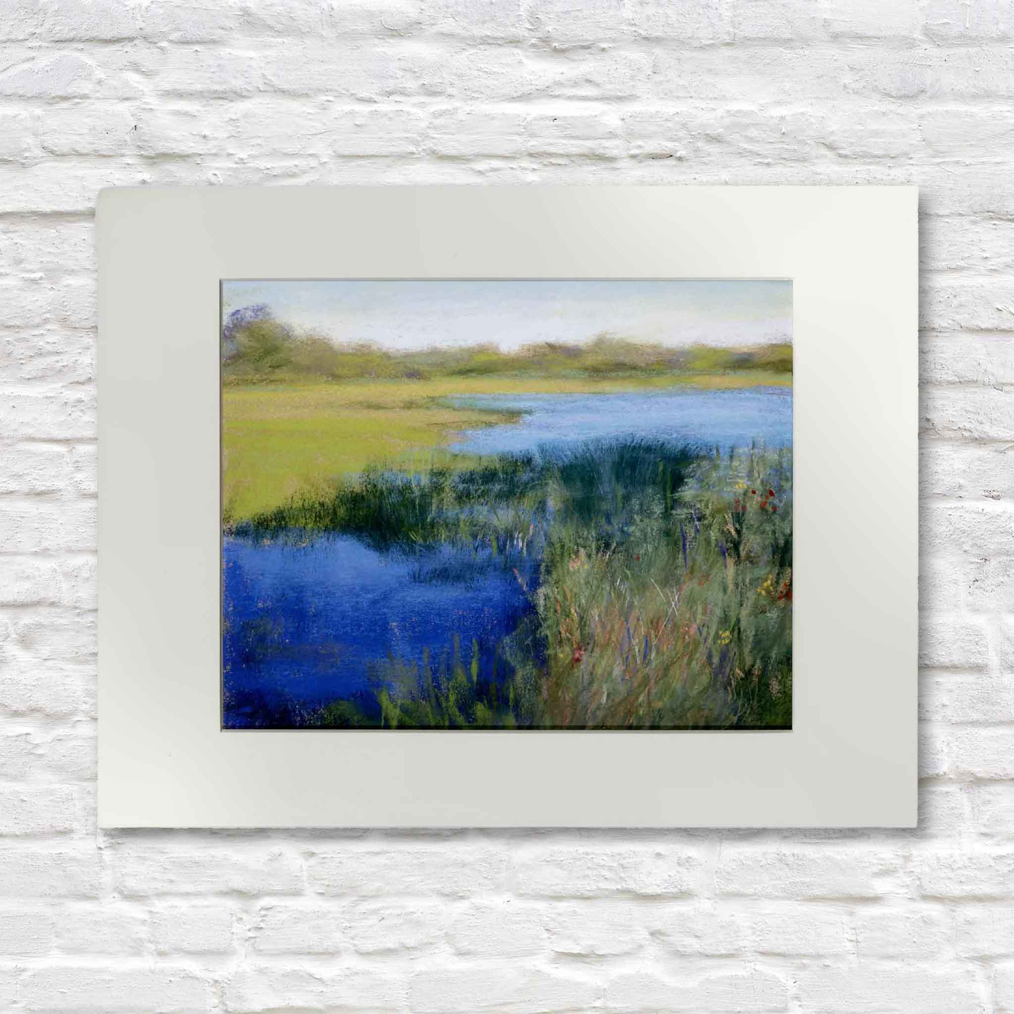 Framed painting of a landscape with a pond and grass on a white brick wall.