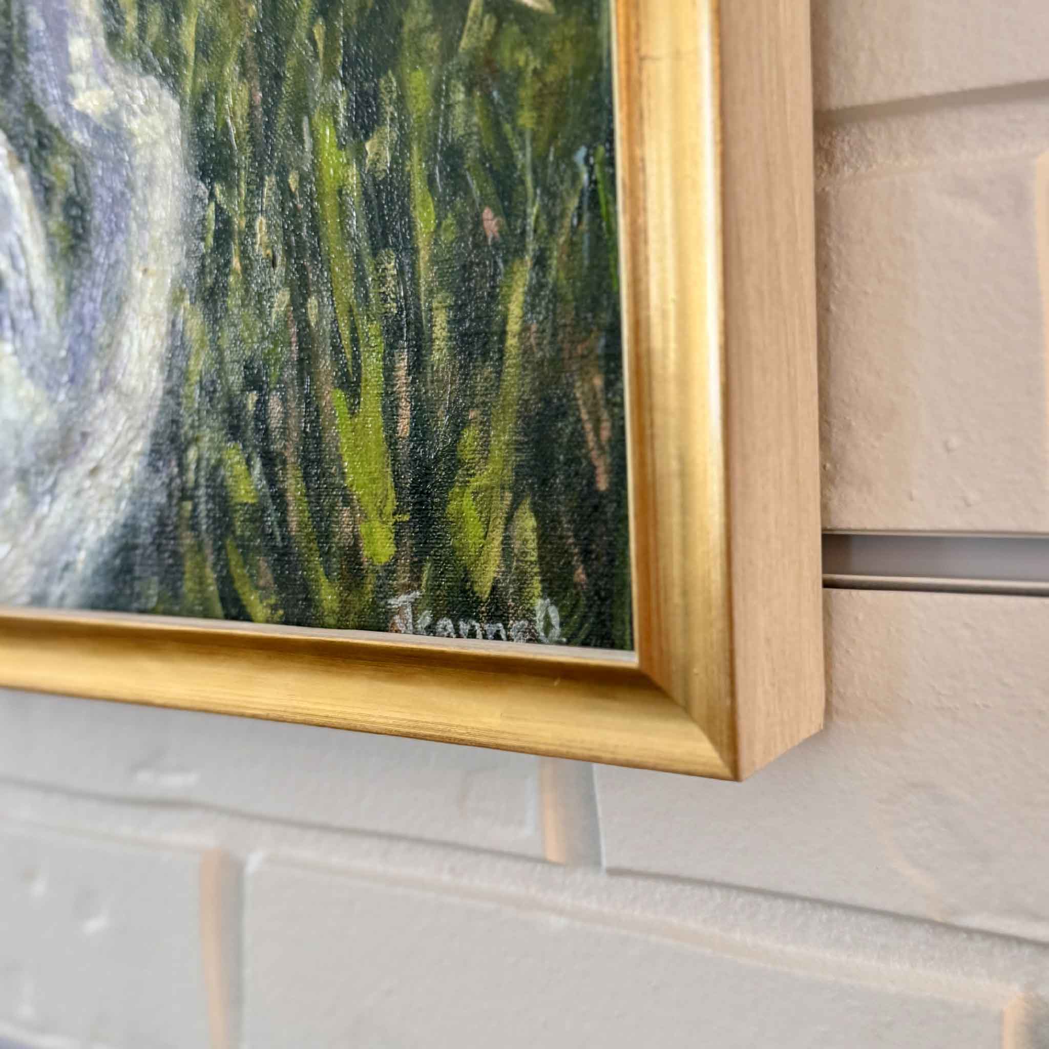 Artist signature on original oil painting in gold frame against white brick wall