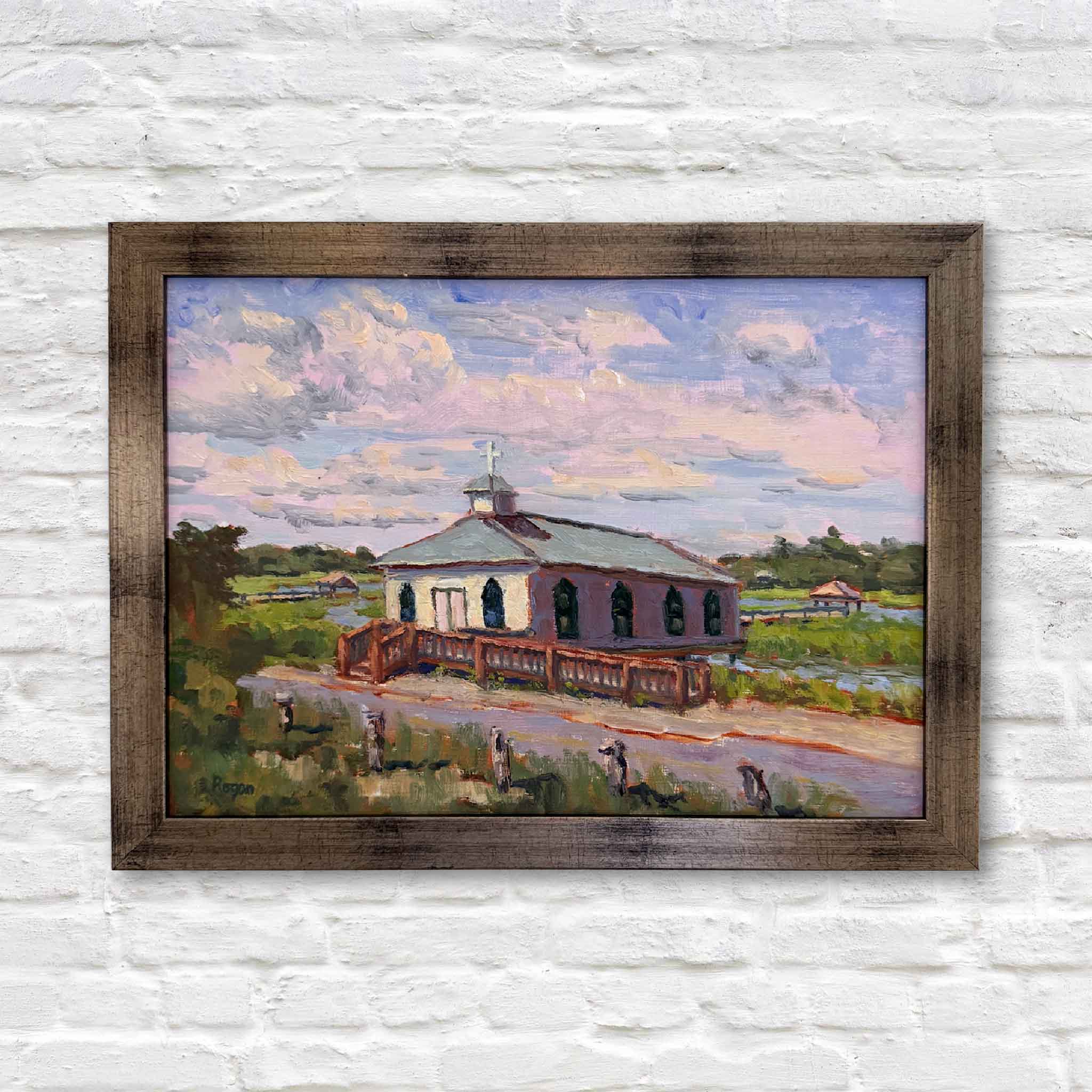Framed painting of a church with a rustic frame on a white brick wall.