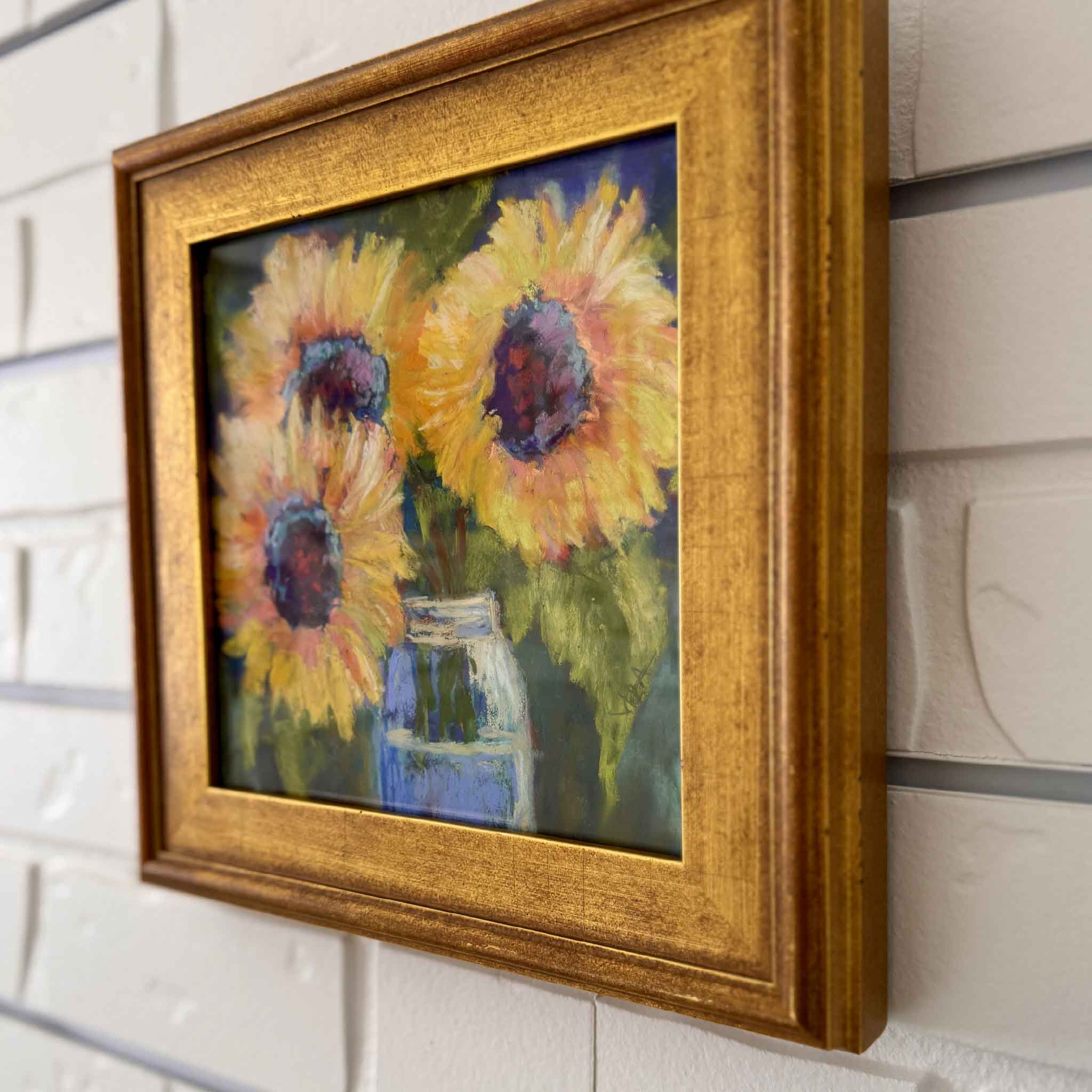 Framed painting of sunflowers in a glass jar on a tiled wall.