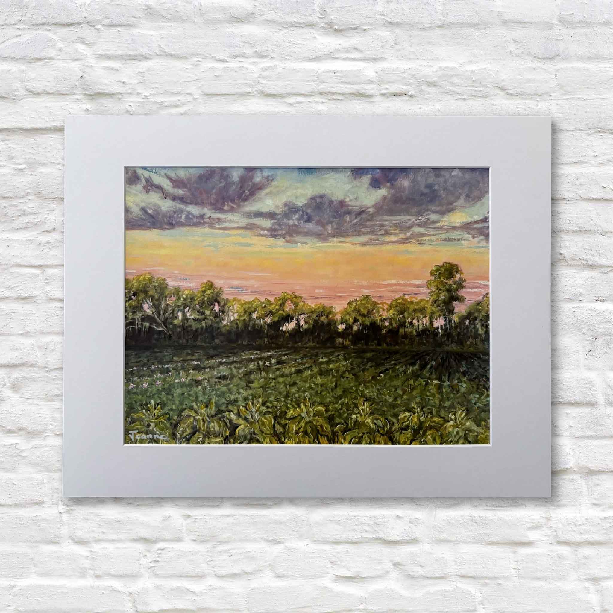 matted artwork of a landscape of tobacco fields with trees and a sunset sky on a white brick wall.