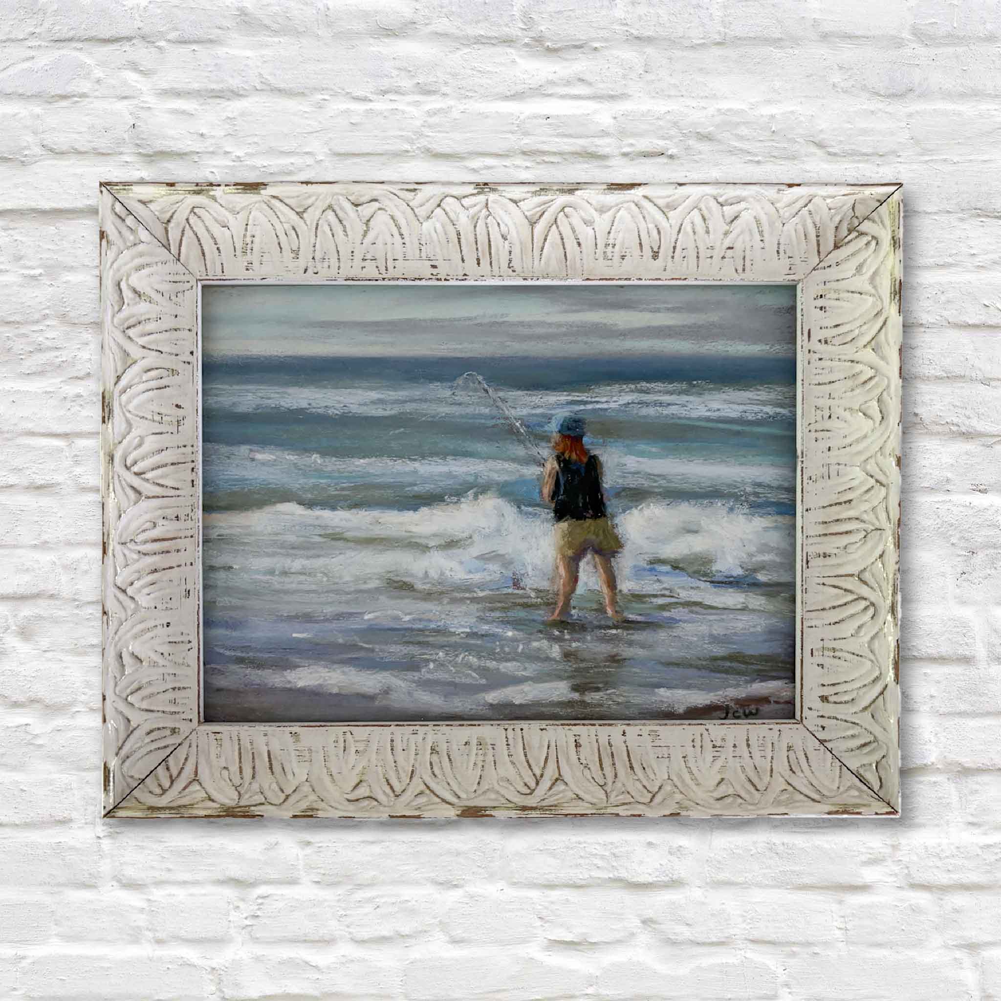 Original pastel painting of a lone surf caster fishing in the ocean waves, framed in a whitewashed carved frame — by Joanne Willoughby.