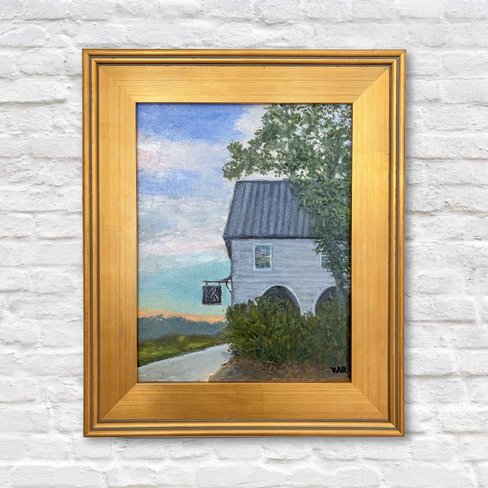Oil painting of The Pelican Inn on Pawleys Island by local artist Kathy Robinson, featuring a historic white inn with a metal roof framed by trees and marsh grasses in soft coastal light, displayed in a gold frame.
