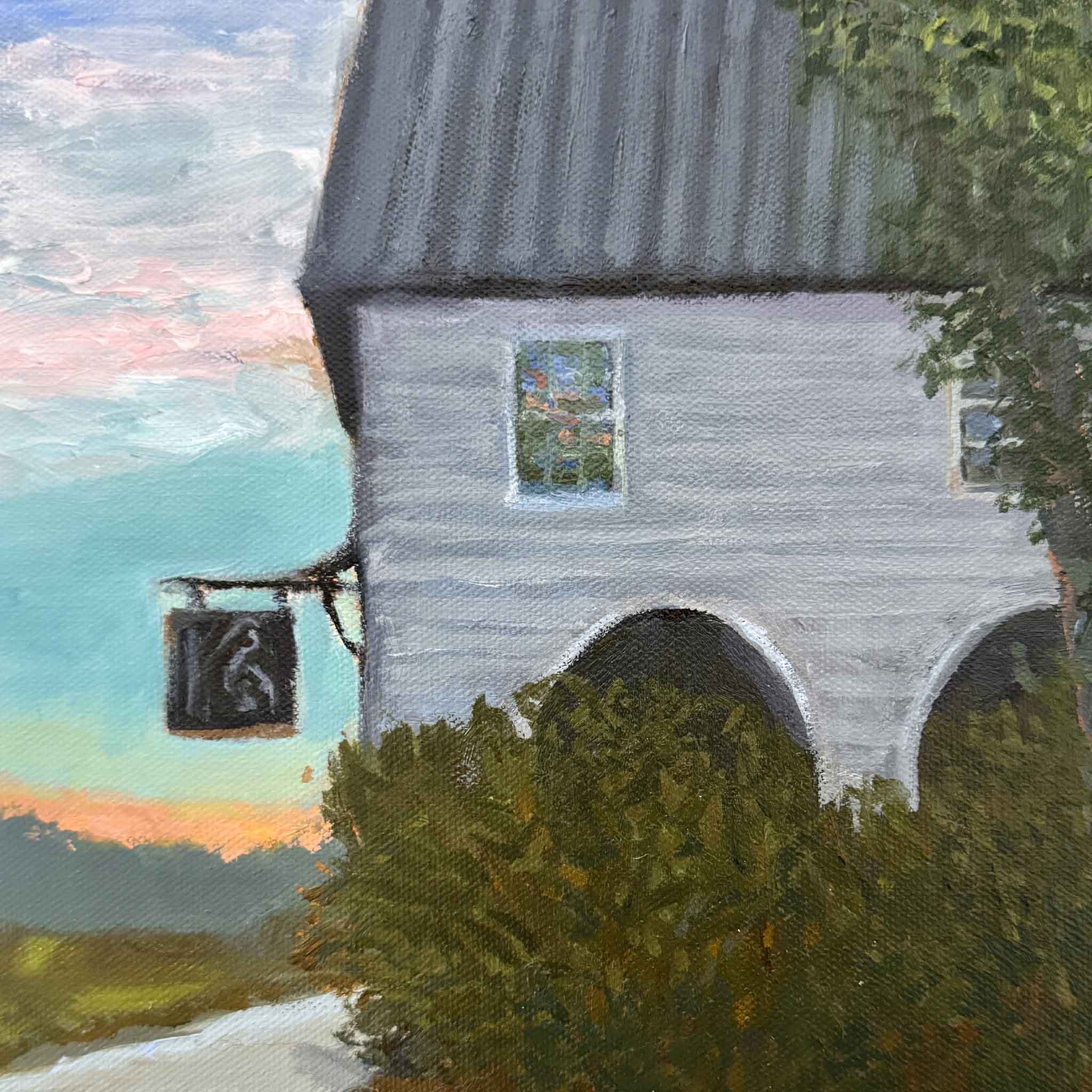 Oil painting of The Pelican Inn on Pawleys Island by local artist Kathy Robinson, featuring a historic white inn with a metal roof framed by trees and marsh grasses in soft coastal light, displayed in a gold frame.