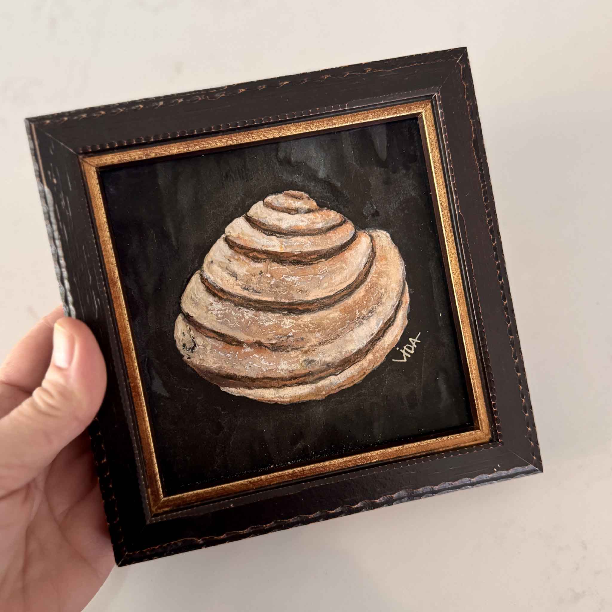 “The Shell” pastel painting by Vida Miller, featuring a Pawleys Island shell on a dark background, framed in black and gold — Lowcountry coastal art.