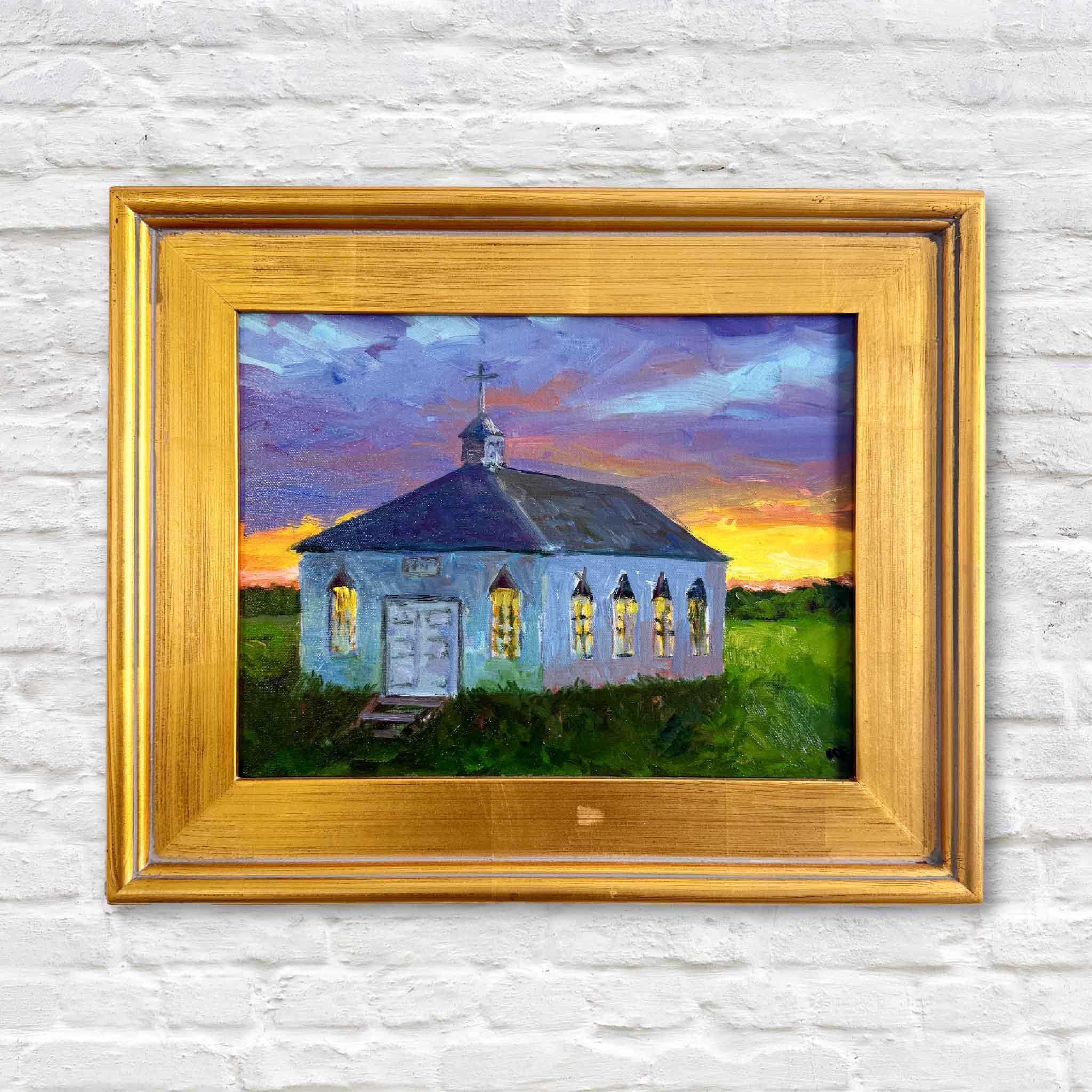Oil painting of Pawleys Island Chapel at sunset by local artist Kathy Robinson, framed in gold. The white chapel glows against a dramatic Lowcountry sky with vivid orange, purple, and blue tones