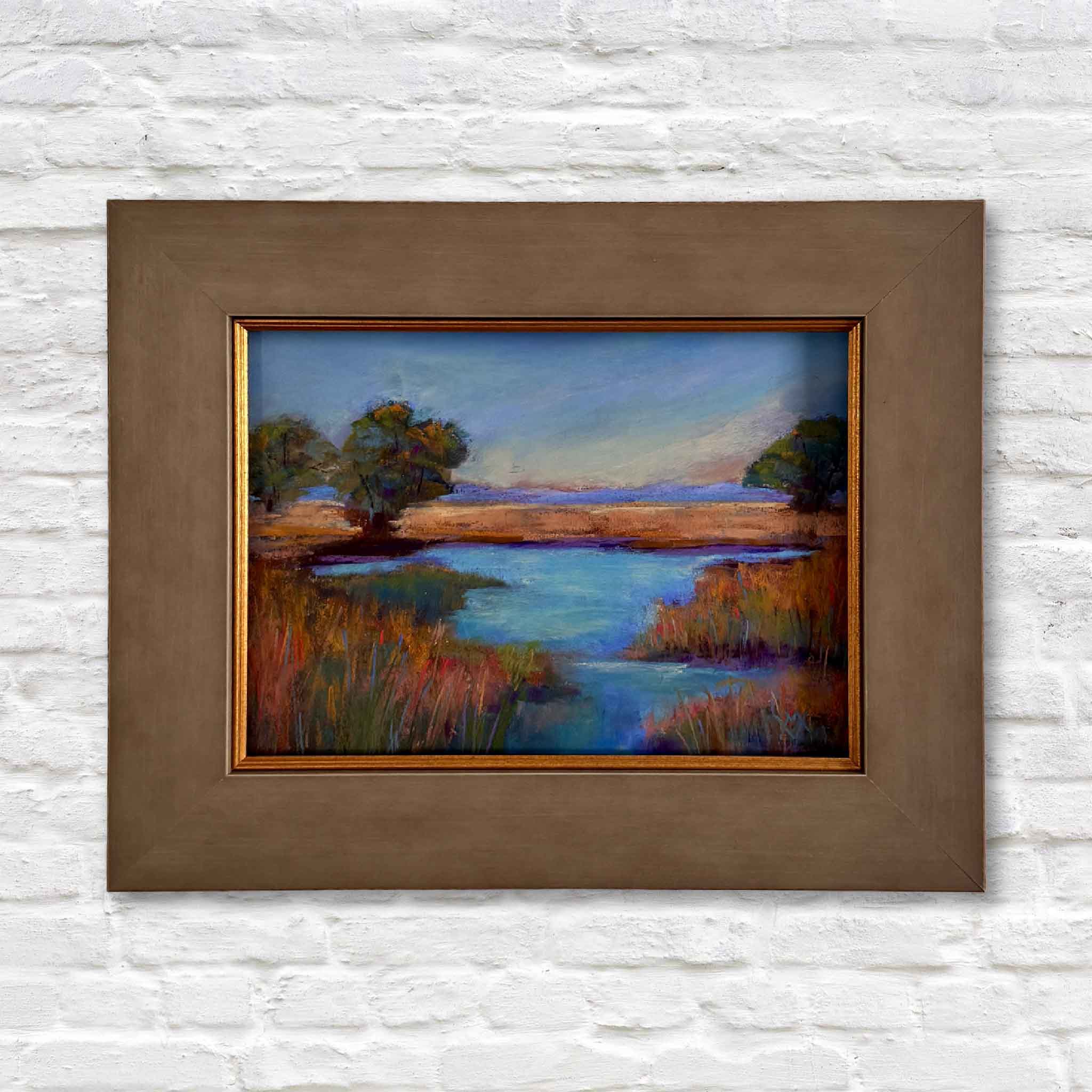 Framed pastel painting of a Lowcountry marsh by Joanne Willoughby, featuring golden grasses, deep blue water, and soft sky tones in a rustic brown frame. Coastal landscape artwork inspired by Pawleys Island and South Carolina marshlands