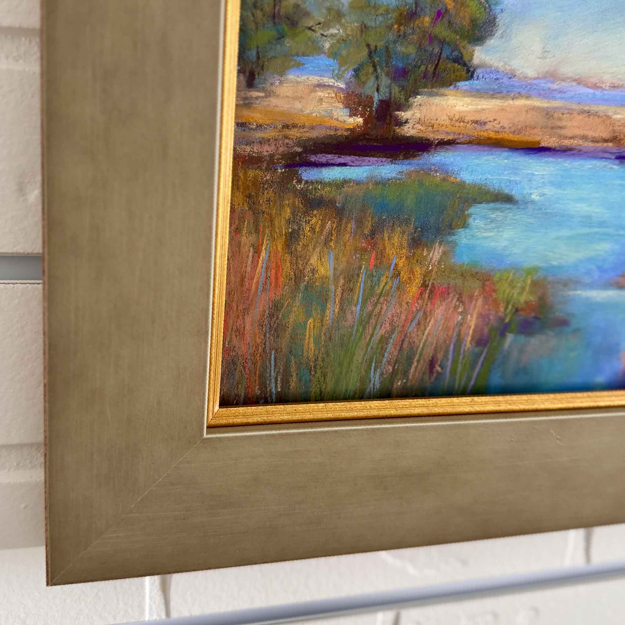 Framed pastel painting of a Lowcountry marsh by Joanne Willoughby, featuring golden grasses, deep blue water, and soft sky tones in a rustic brown frame. Coastal landscape artwork inspired by Pawleys Island and South Carolina marshlands