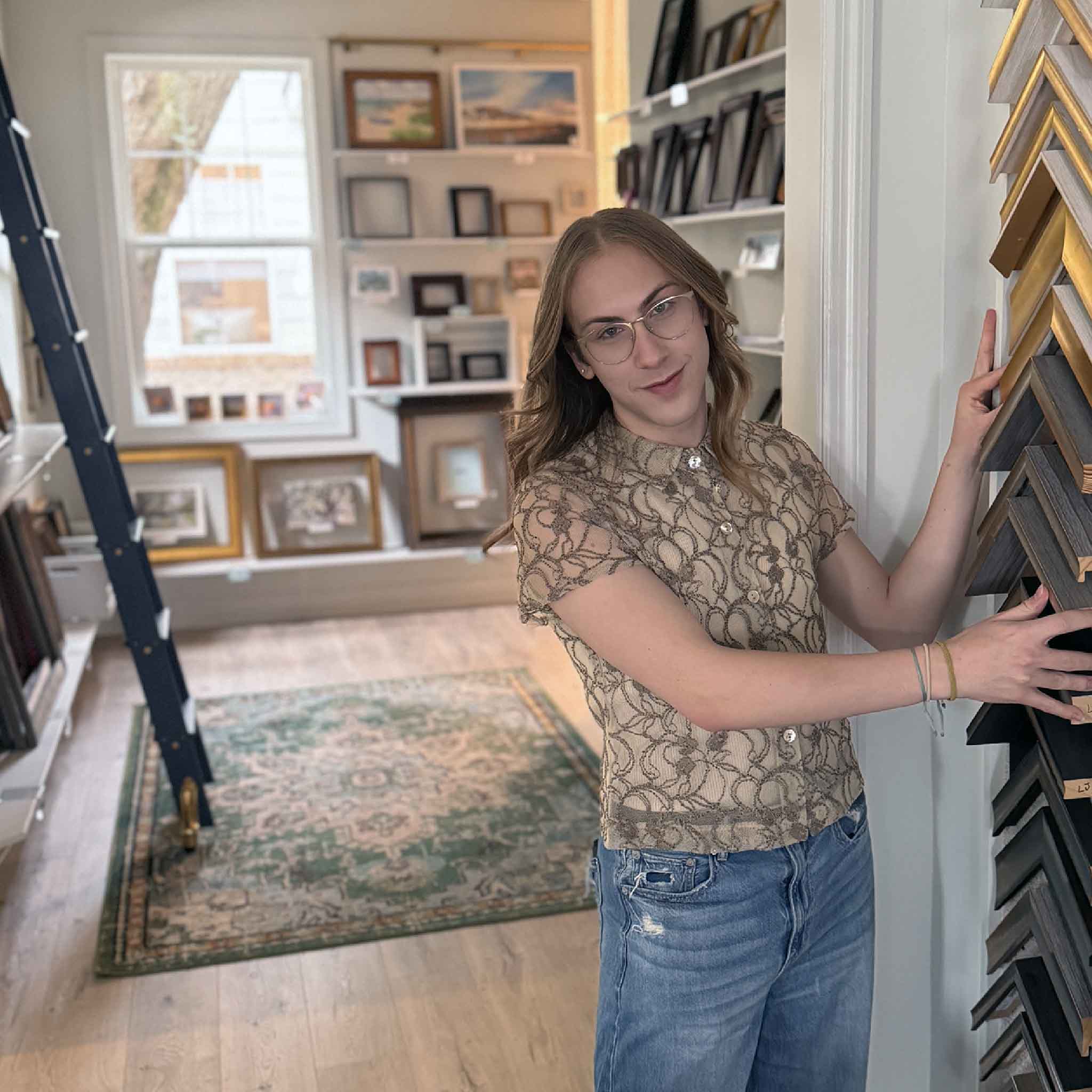 Alex, a team member at Gray Man Gallery, standing in the framing studio beside a wall of frame samples.