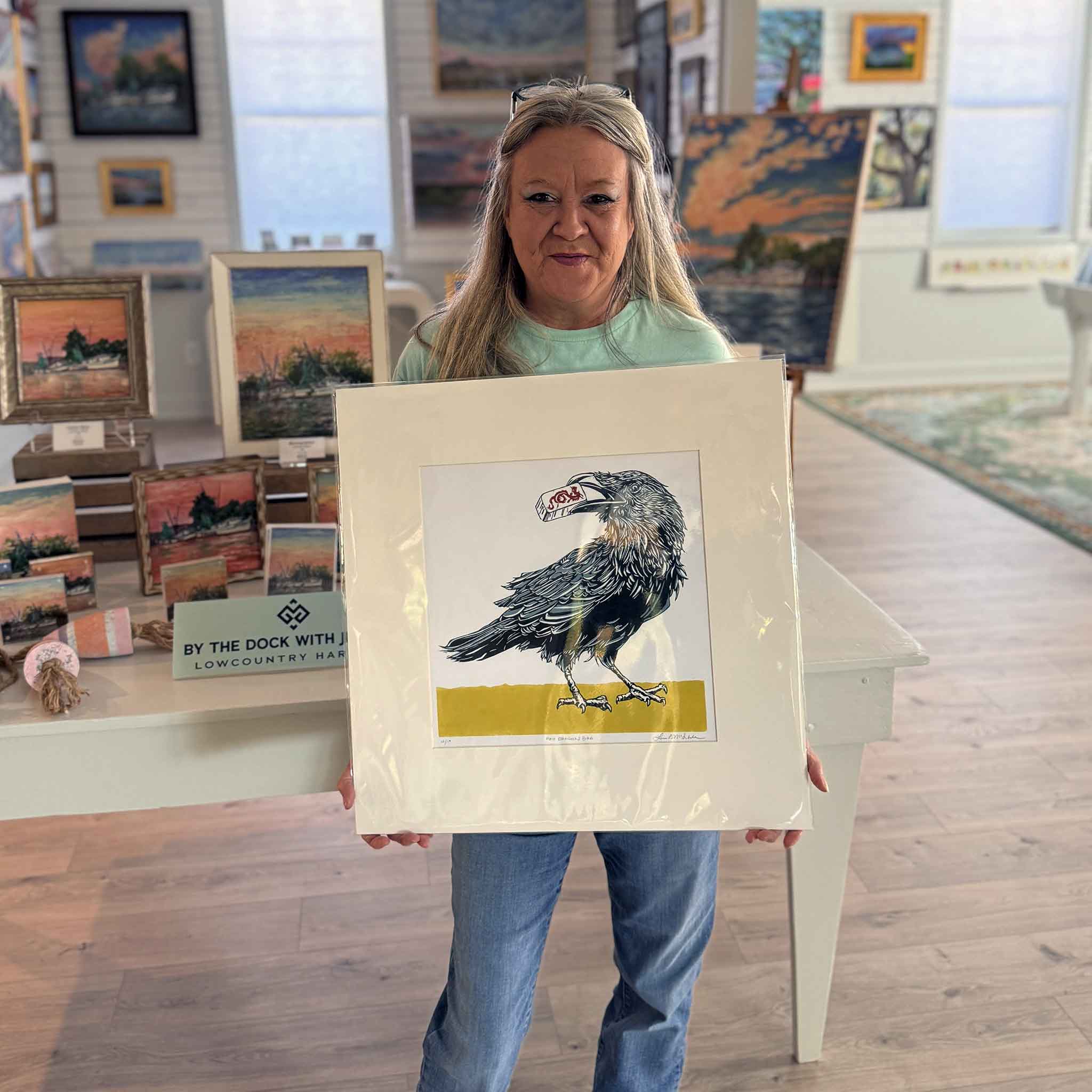 Custom framer holding original linocut by Laurie McIntosh of a blackbird holding a Red Dragon mahjong tile, signed and numbered, matted to 20×20 inches