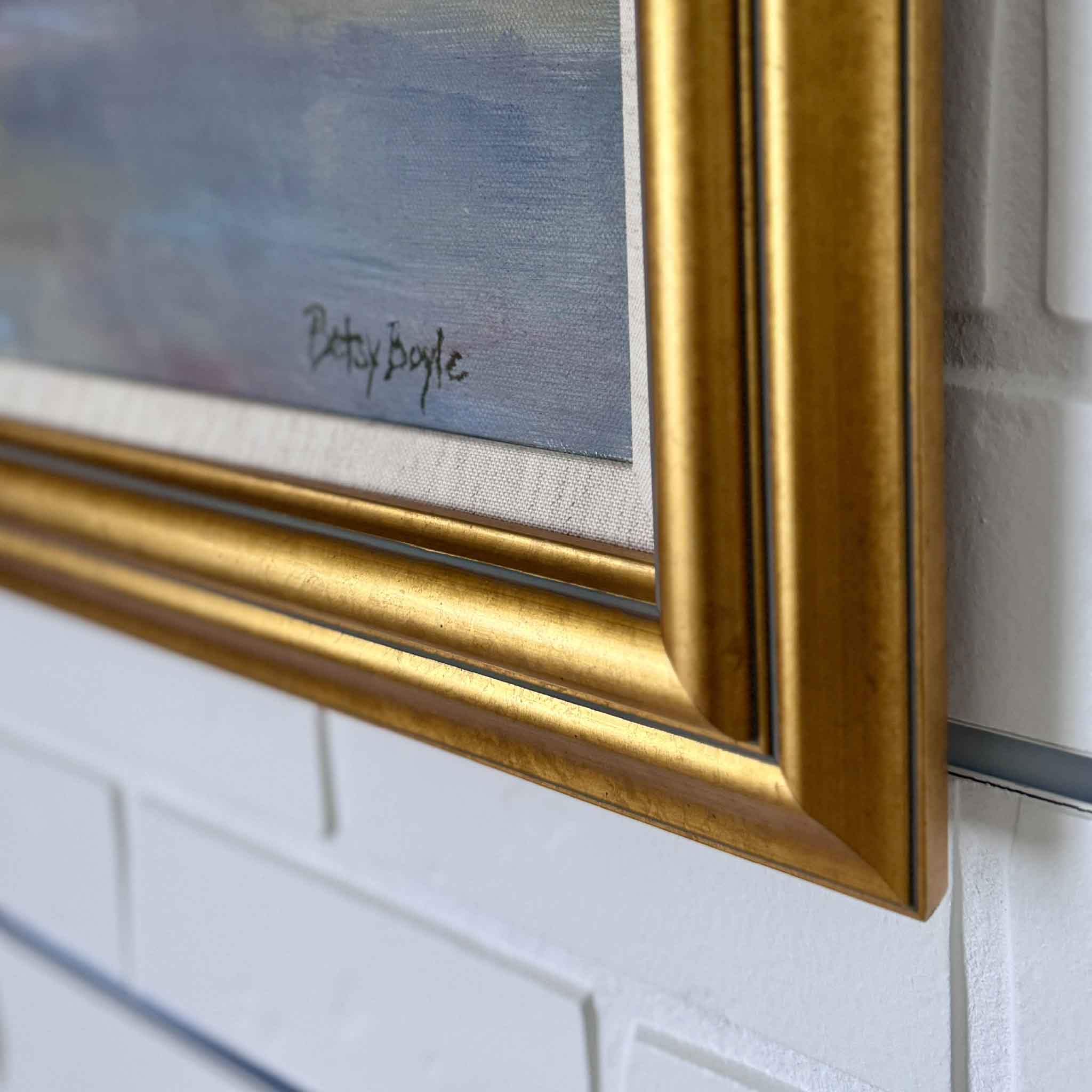 Gold-framed painting with a signature on a white brick wall