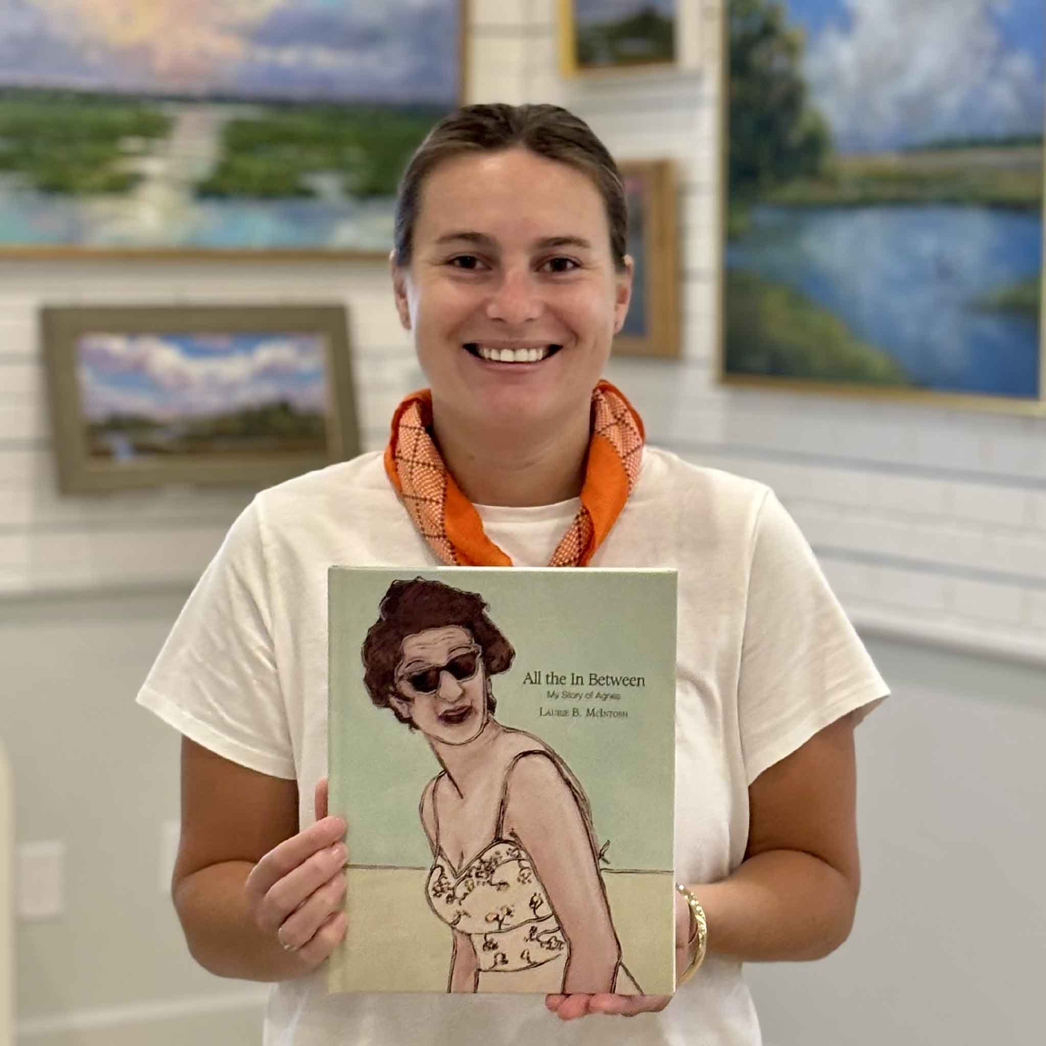 Kyra displays a signed copy of "All the In Between: My Story of Agnes" by Laurie Brownell McIntosh at Gray Man Gallery. This hardcover memoir blends artwork and storytelling to celebrate the life of Agnes Smith Brownell and includes full-color paintings throughout.