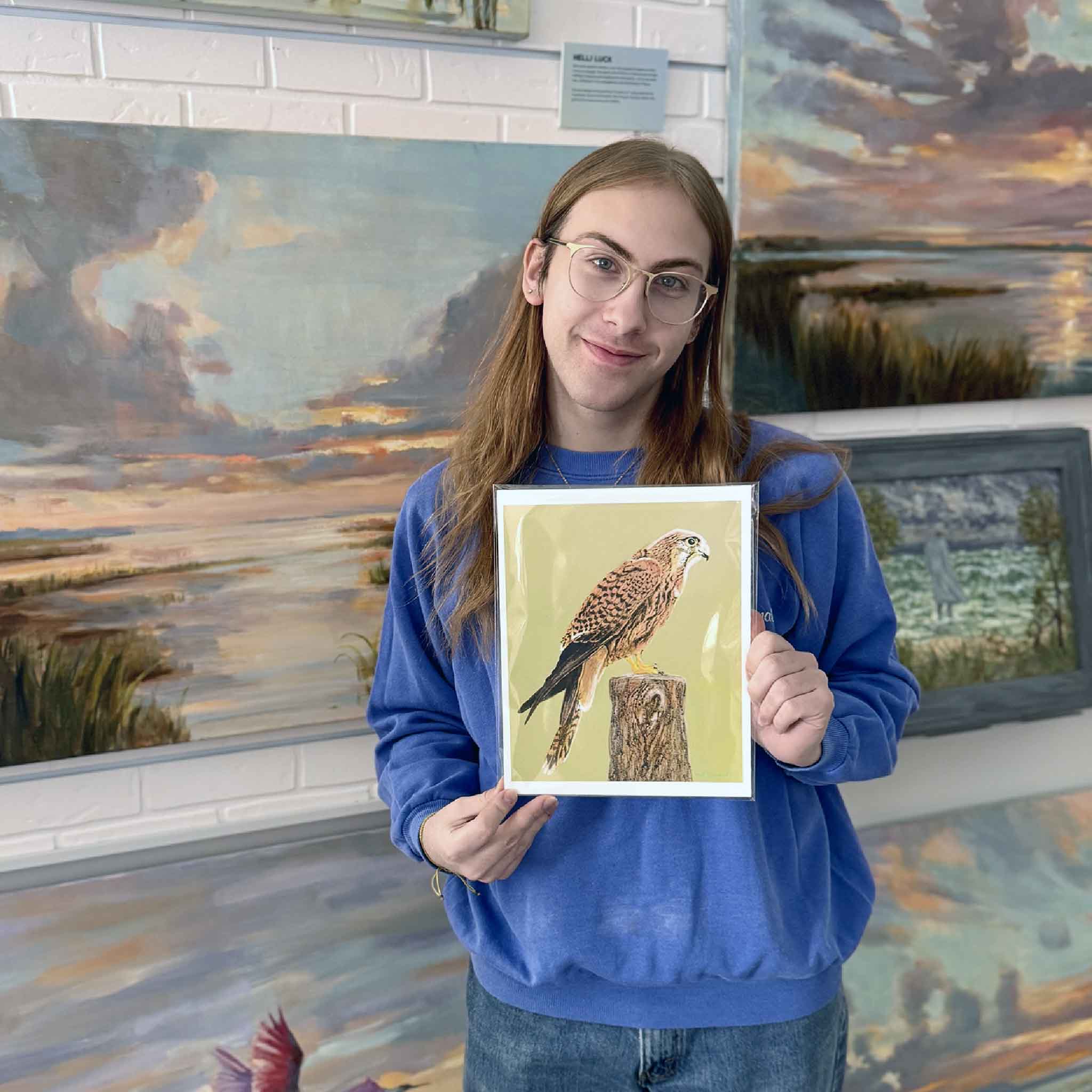 A Gray Man Gallery team member holds American Kestrel Study by Mimi Beaver, a wildlife artwork donated to benefit Salty Dogs Senior Animal Rescue with 100 percent of proceeds supporting senior dogs.
