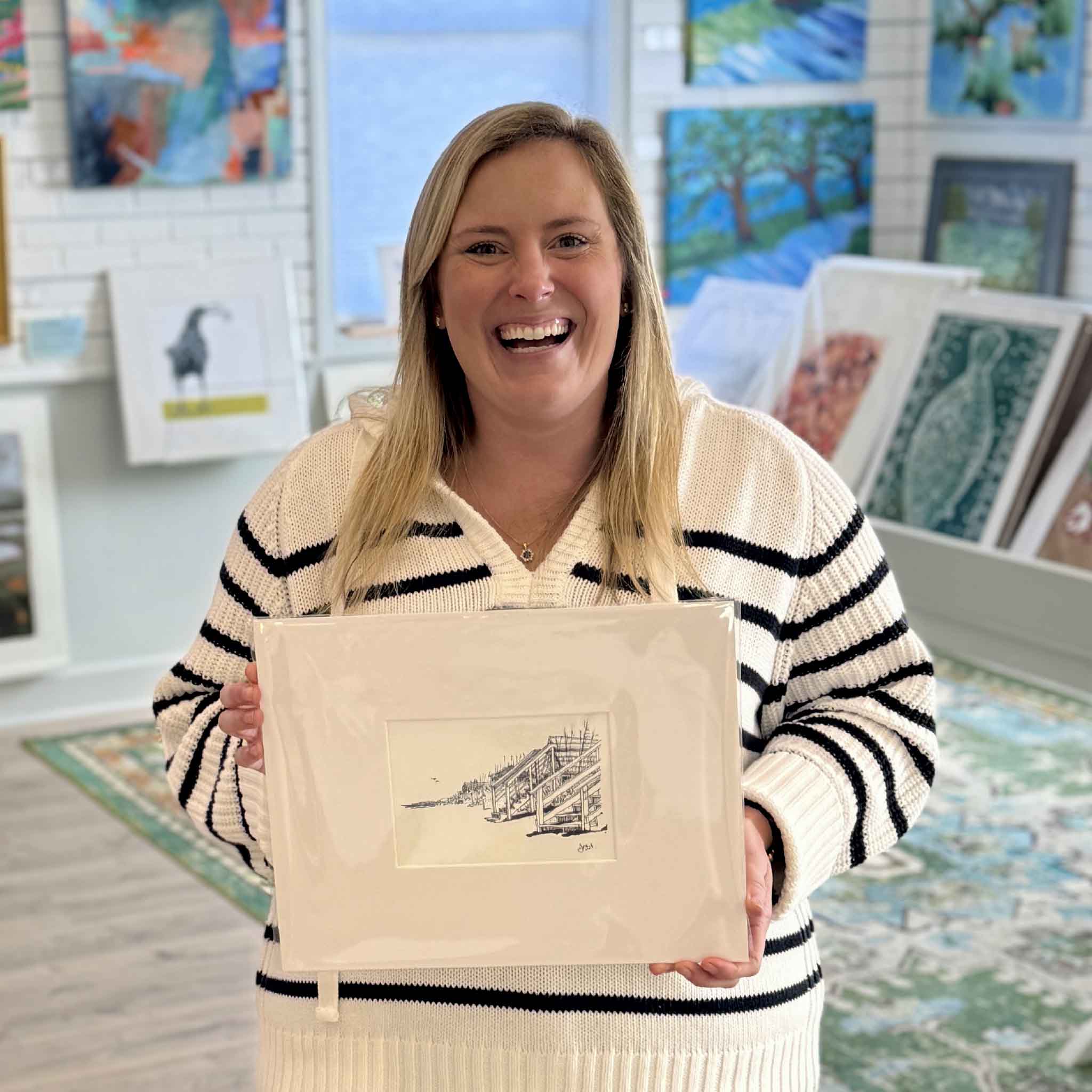 Bordy holding local Lowcountry artist Todd Halamka's  pen-and-ink print “Beach Front Stairs” inside Gray Man Gallery in Pawleys Island, South Carolina, showcasing a coastal boardwalk drawing professionally matted and ready to frame.