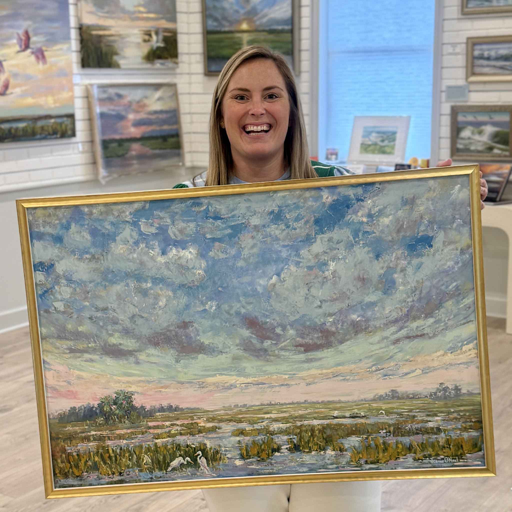 Gray Man Gallery staff member Bordy holding Beneath the Blushing Sky original oil painting by Jeanne O’Neal in Pawleys Island South Carolina art gallery
