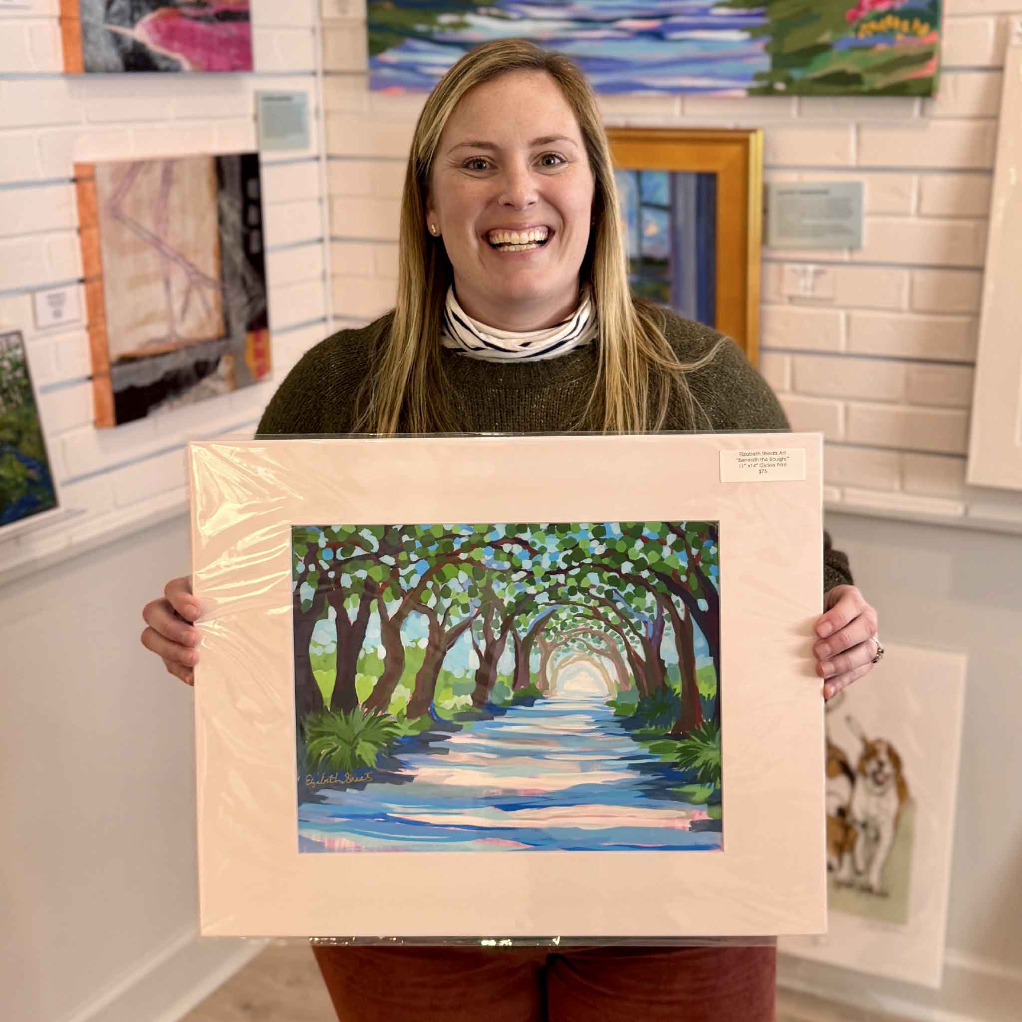 Bordy holding Elizabeth Sheats Beneath the Boughs 16x20 fine art giclée print at Gray Man Gallery in Pawleys Island South Carolina, featuring live oak tunnel, oak-lined driveway, and serene Lowcountry plantation landscape artwork