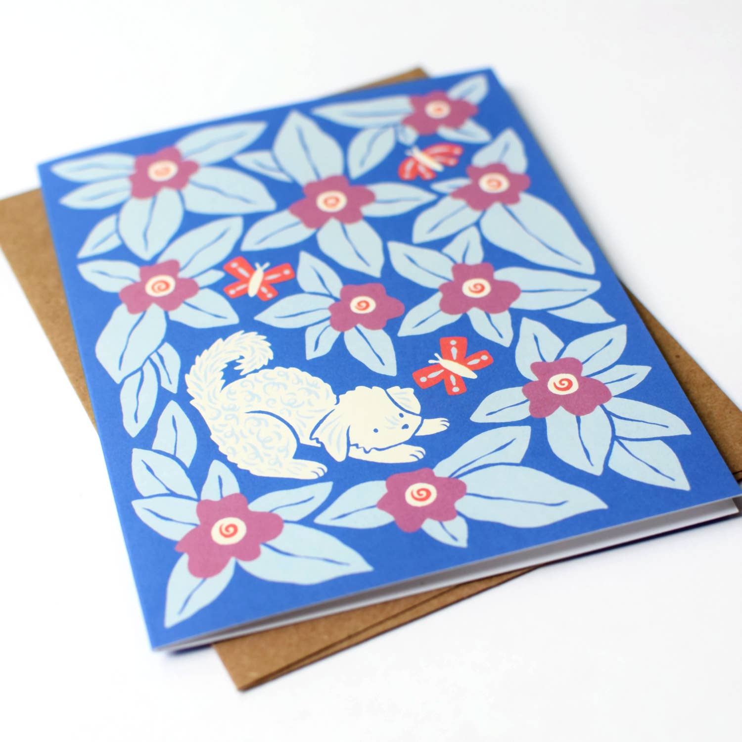Open view of the Bennie Blooms greeting card by Chrissie Van Hoever displayed with its recycled kraft envelope, highlighting the premium recycled cardstock and whimsical floral dog illustration available at Gray Man Gallery in Pawleys Island, South Carolina.