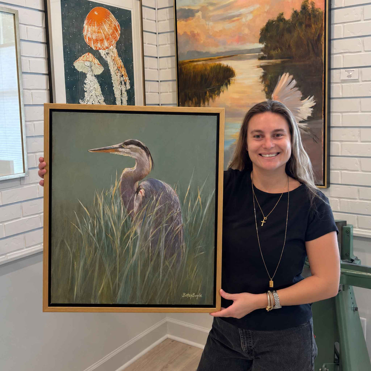 Cool Light original great blue heron oil painting by local artist Betsy Boyle shown at Gray Man Gallery in Pawleys Island, South Carolina, featuring a blue-gray heron surrounded by tall coastal marsh grass in a warm wood frame