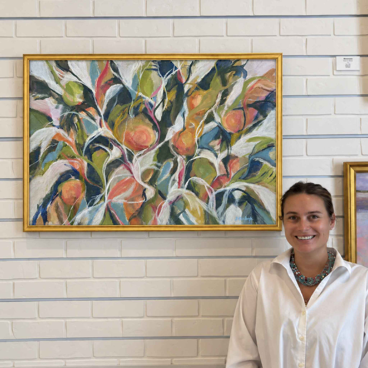Fruitful in Coral original oil painting by South Carolina artist Betsy Boyle displayed at Gray Man Gallery in Pawleys Island, showing the scale of the horizontal botanical artwork with layered coral fruit, green foliage, blue-gray leaves and sweeping white branches in a gold frame