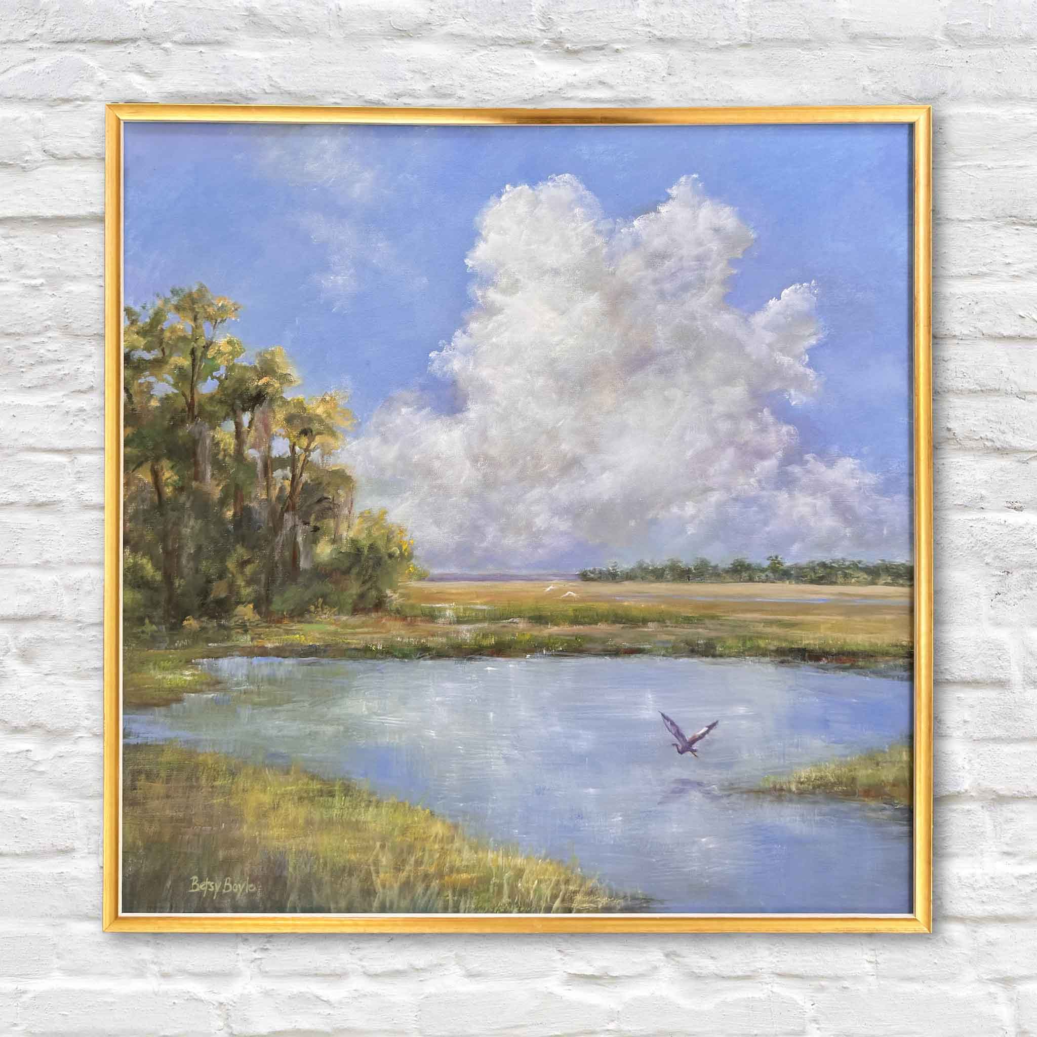 Just Breathe by Betsy Boyle original oil painting featuring a serene Lowcountry marsh landscape with expansive blue sky, towering white clouds, reflective water, and a bird in motion, framed in gold and photographed at Gray Man Gallery in Pawleys Island, South Carolina, showcasing the artist’s soft atmospheric brushwork and coastal subject matter