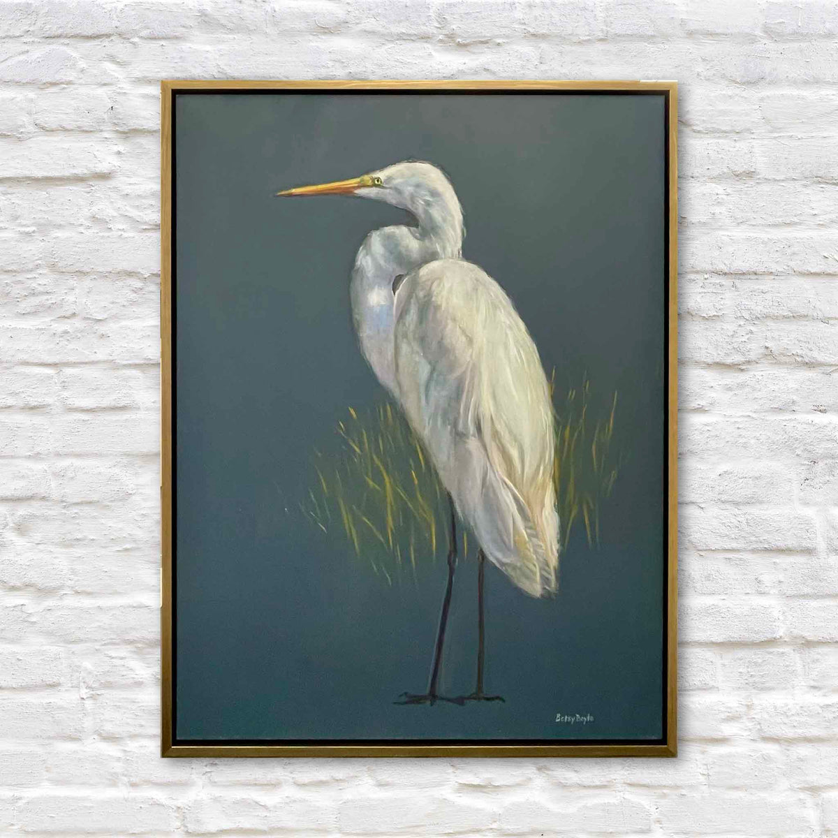 Proud original oil painting by South Carolina artist Betsy Boyle featuring a great egret with luminous white plumage standing against a deep blue-green background with subtle marsh grasses, framed in warm gold and available at Gray Man Gallery in Pawleys Island, South Carolina