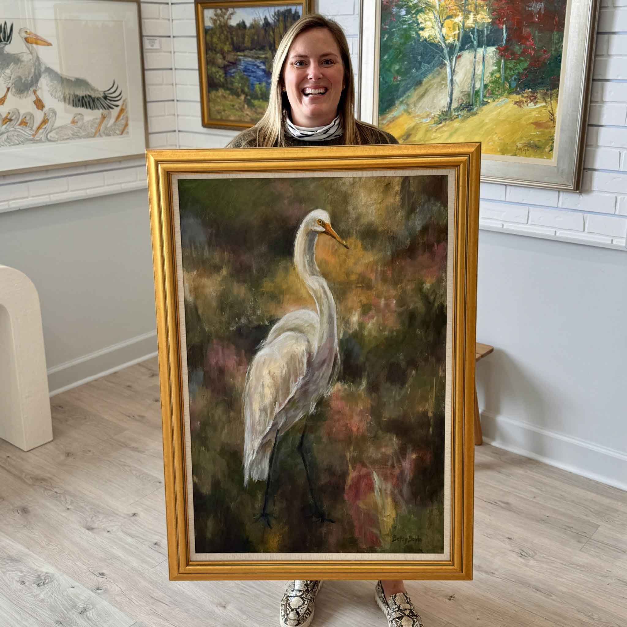Betsy Boyle original egret painting “Watching” displayed at Gray Man Gallery in Pawleys Island, South Carolina, held by gallery staff to show scale and professional framing