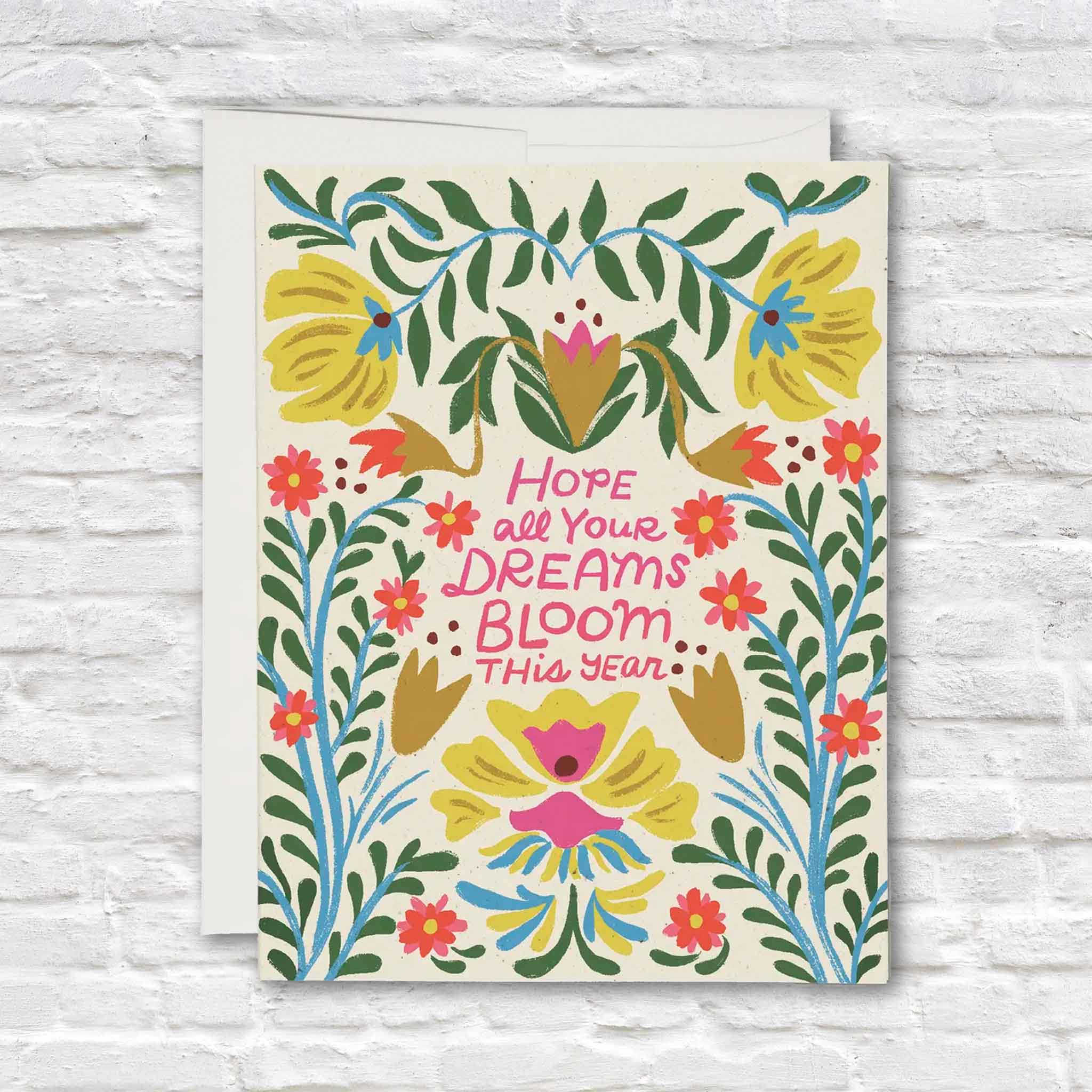 Blooming Dreams greeting card illustrated by Dylan Mierzwinski featuring colorful folk-art-inspired flowers, leafy botanical vines, and the uplifting message "Hope all your dreams bloom this year." This blank-inside Red Cap Cards greeting card is available at Gray Man Gallery in Pawleys Island, South Carolina and is perfect for birthdays, graduations, new beginnings, encouragement, congratulations, and thoughtful everyday gifting.