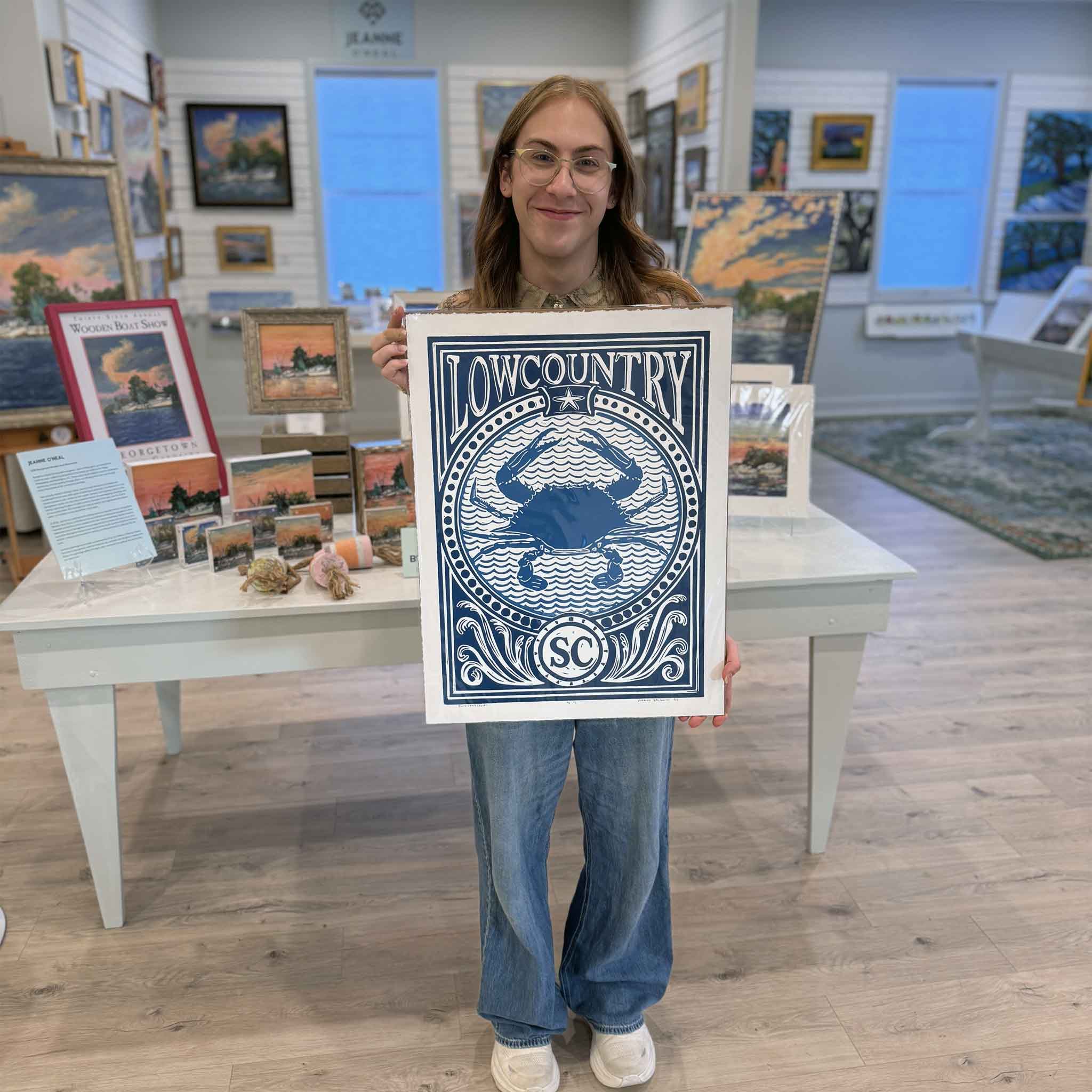 Alex holding the blue Blue Crab linocut print by Aaron Baldwin inside Gray Man Gallery.