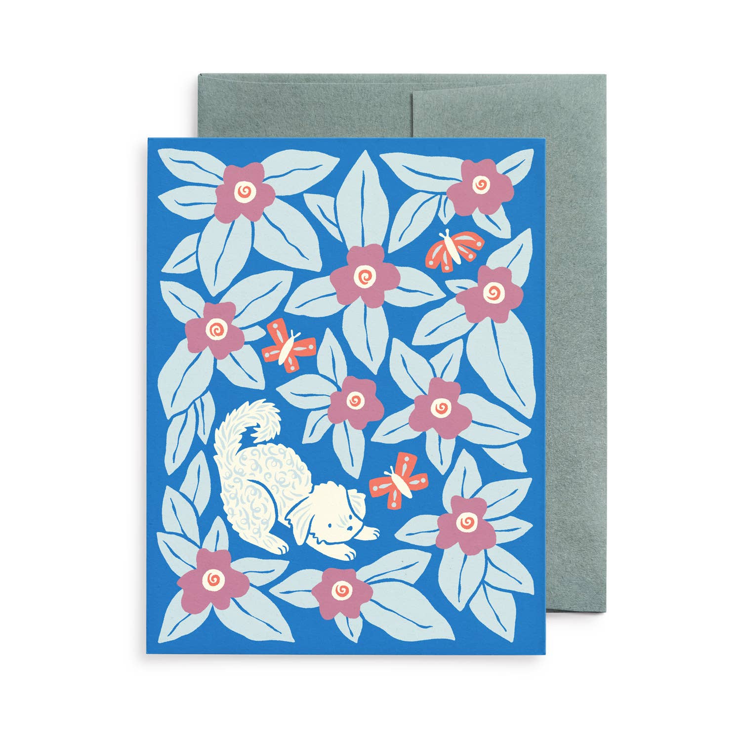 Blank greeting card featuring an original illustration by Chrissie Van Hoever of a playful white puppy exploring vibrant blue flowers with pink blossoms and butterflies. Printed on premium recycled paper with a coordinating kraft envelope and available individually or as part of the Dogs & Blooms card collection at Gray Man Gallery in Pawleys Island.
