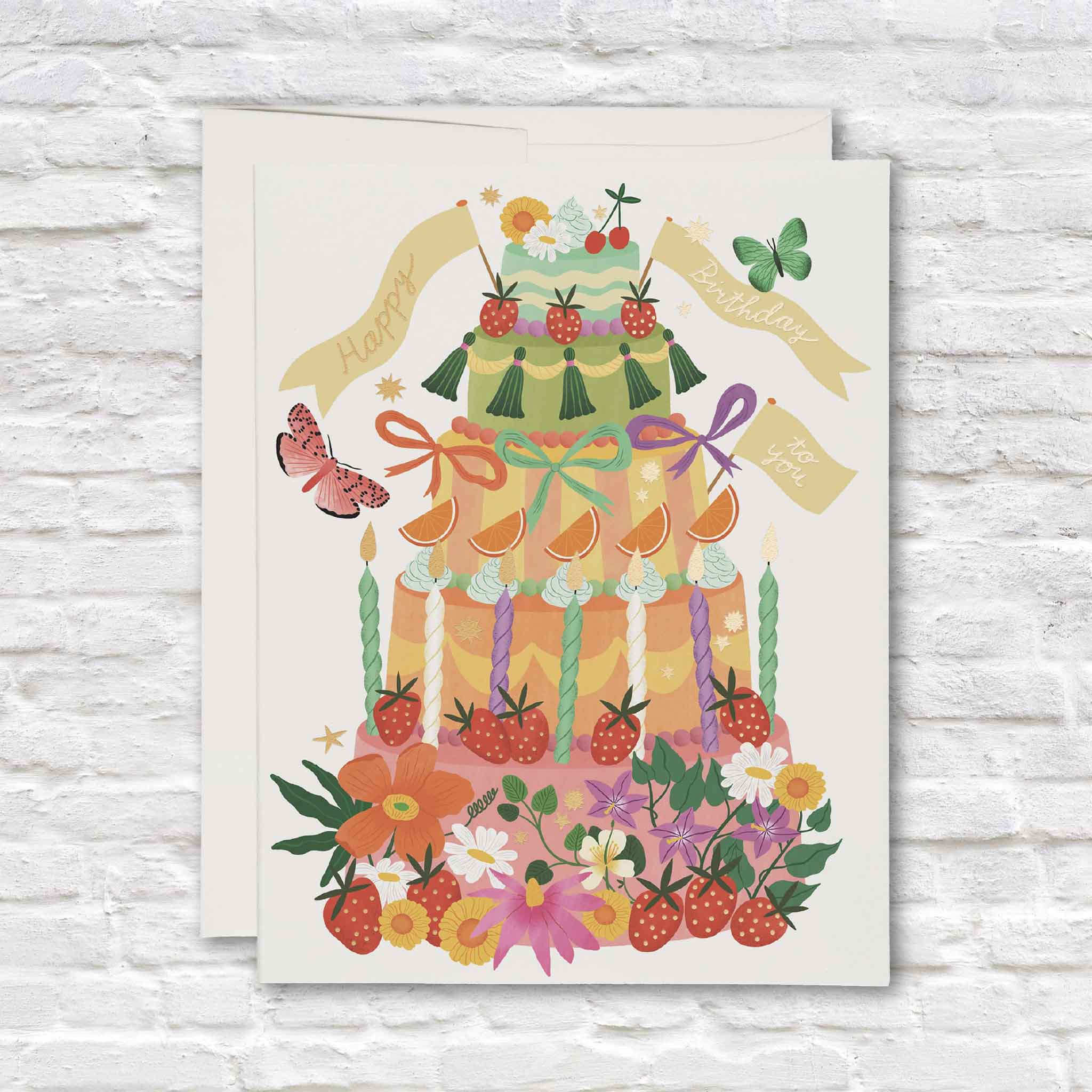 Whimsical Cake birthday card illustrated by Bodil Jane for Red Cap Cards, featuring a colorful three-tier cake covered in strawberries, flowers, ribbons, candles, cherries, butterflies and gold foil details, available inside Gray Man Gallery in Pawleys Island, South Carolina.