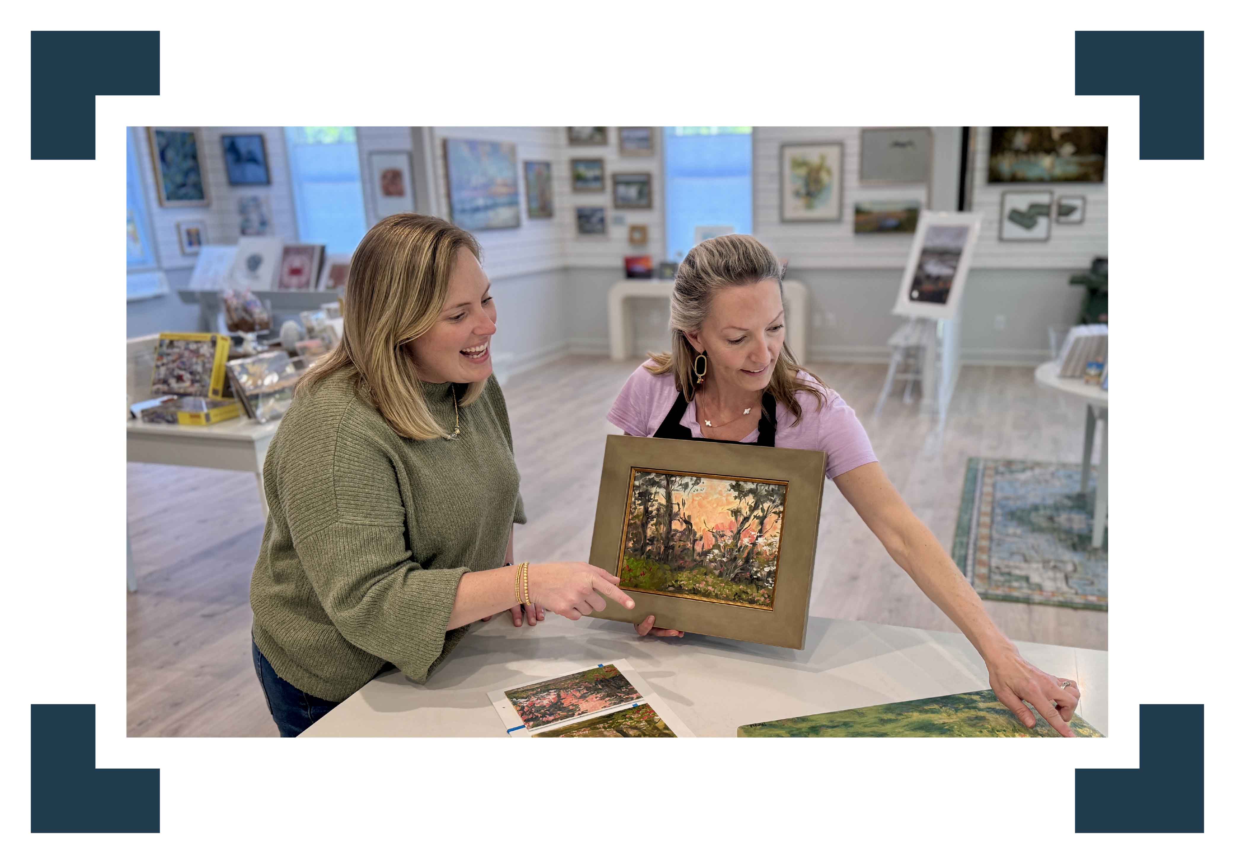 Bordy and local Lowcountry artist Jeanne O’Neal review framing options together at Gray Man Gallery in Pawleys Island, South Carolina, as Jeanne holds a small original landscape painting in a warm gold frame while Bordy points to artwork on the table, illustrating the gallery’s personalized, boutique-style custom framing process surrounded by original coastal artwork and fine art prints