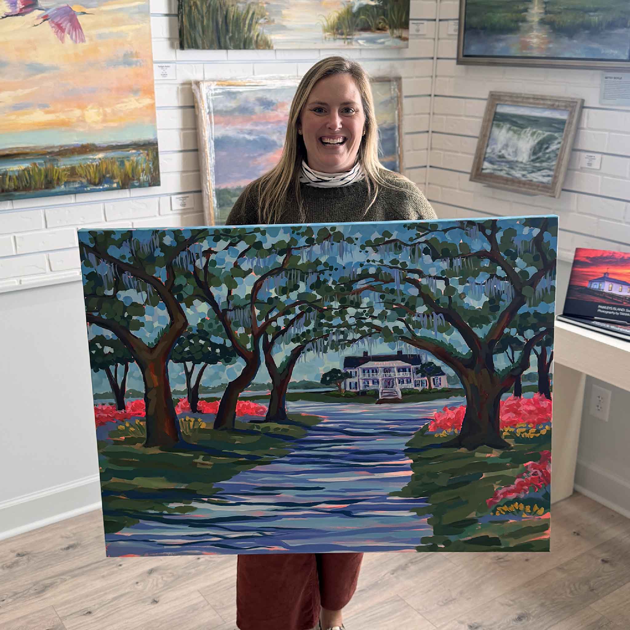 Gray Man Gallery staff member Bordy holding “Azaleas at Litchfield” original painting by Elizabeth Sheats inside the Pawleys Island gallery, showing scale, color, and Lowcountry landmark artwork