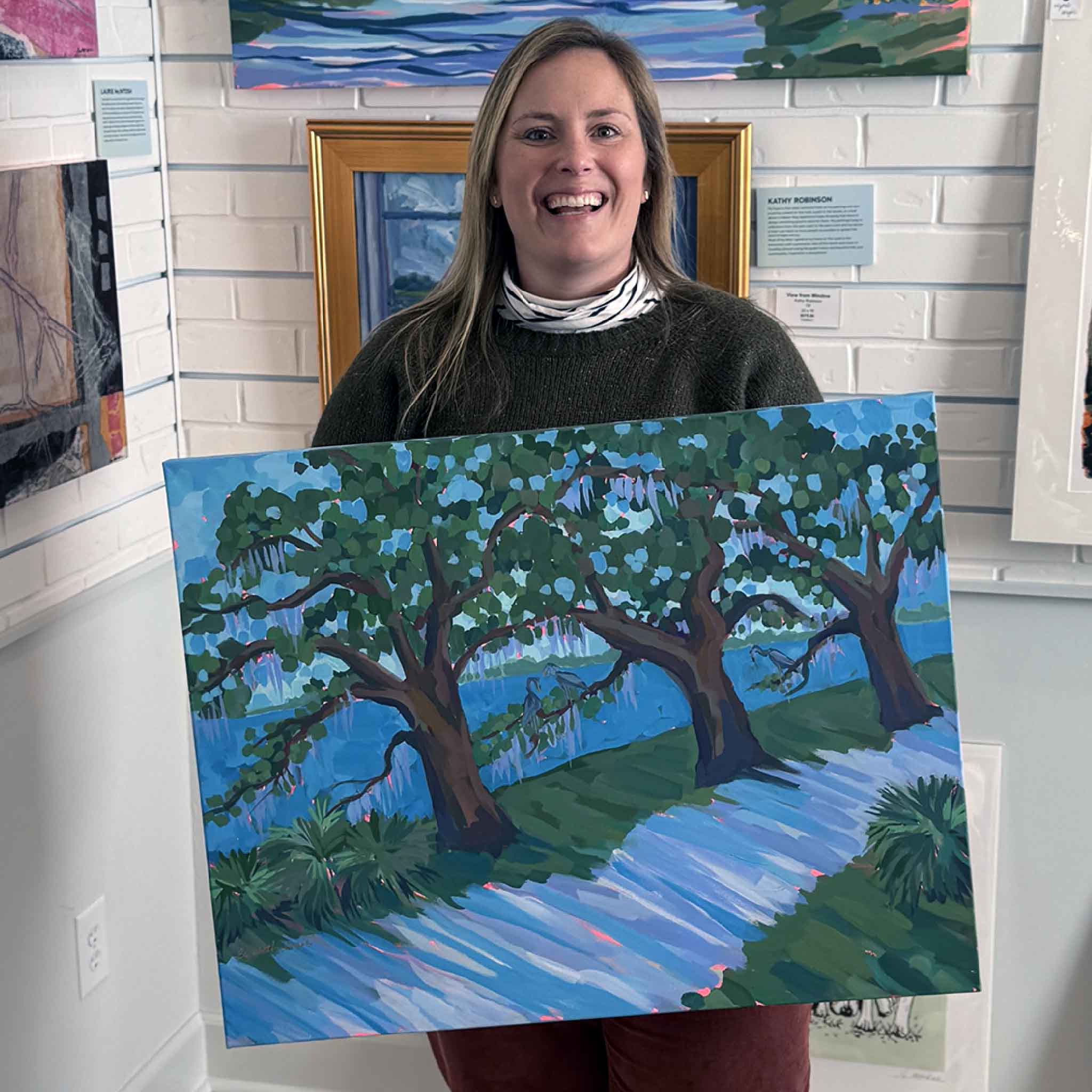 Gray Man Gallery team member Bordy holding the original painting Canopy Walk II by Elizabeth Sheats inside the Pawleys Island gallery showcasing local Lowcountry artwork