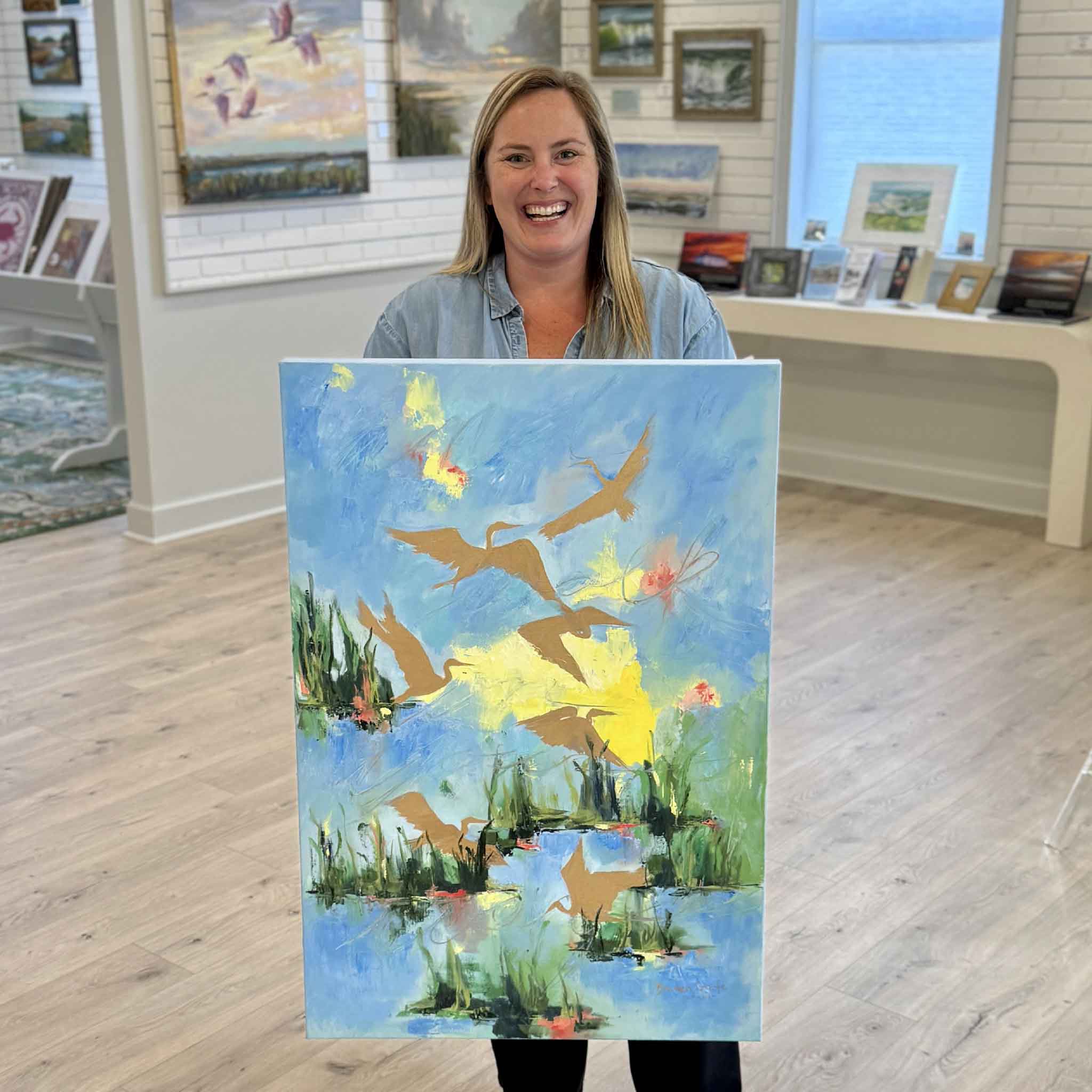 Bordy holding Delight, an original oil painting by local Lowcountry artist Braden Grafe at Gray Man Gallery in Pawleys Island, South Carolina, featuring soaring birds, luminous marsh waters, and vibrant coastal colors
